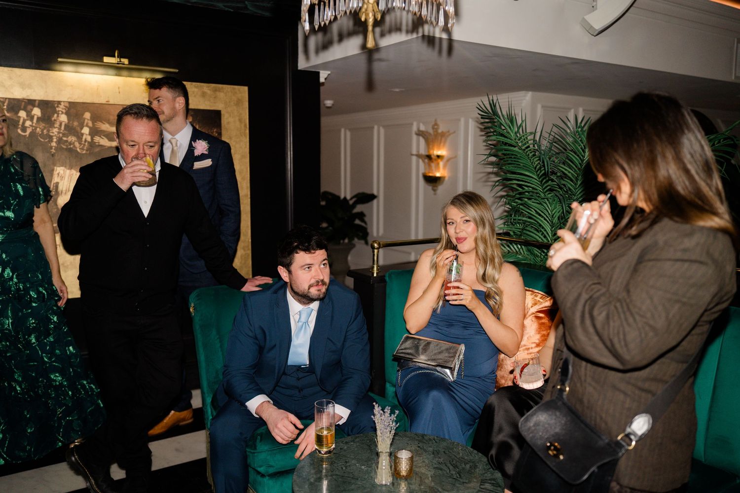 Wedding guests socializing in stylish green-themed bar lounge during evening reception.