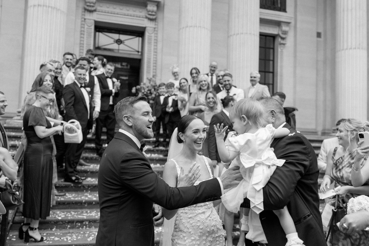 Wedding celebration sequence outside a classical building with columns and scattered flower petals.
