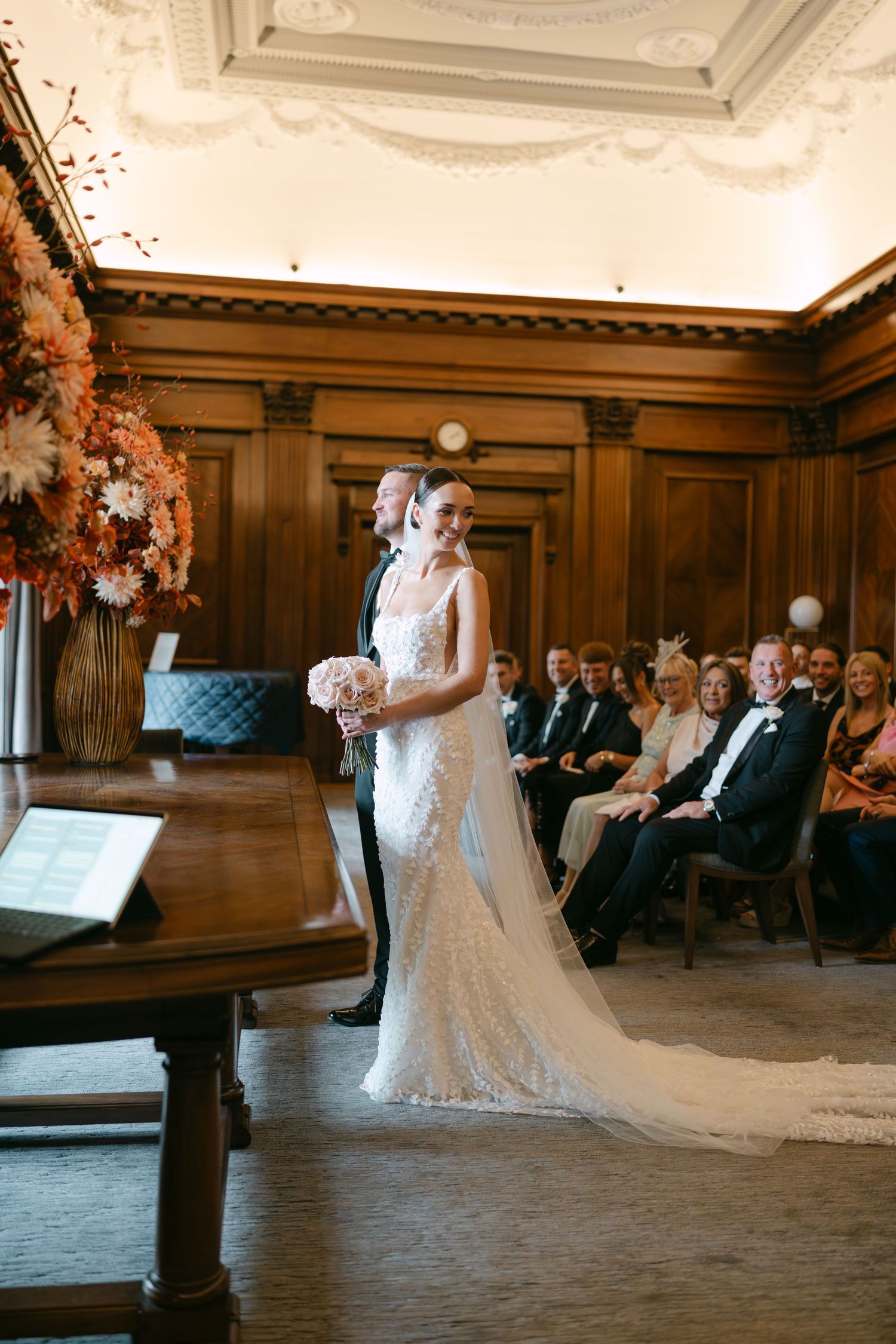 Wedding celebration in a grand hall with ornate ceiling details and wood paneling.