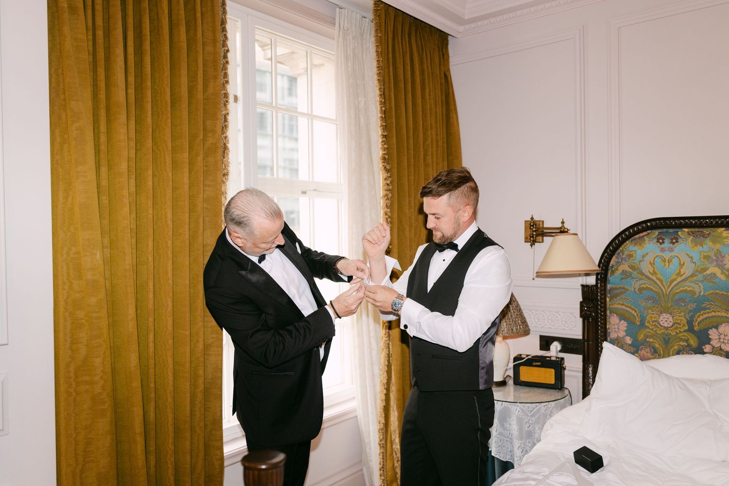 Two people in formal attire toasting with champagne glasses in an elegant room with golden curtains.