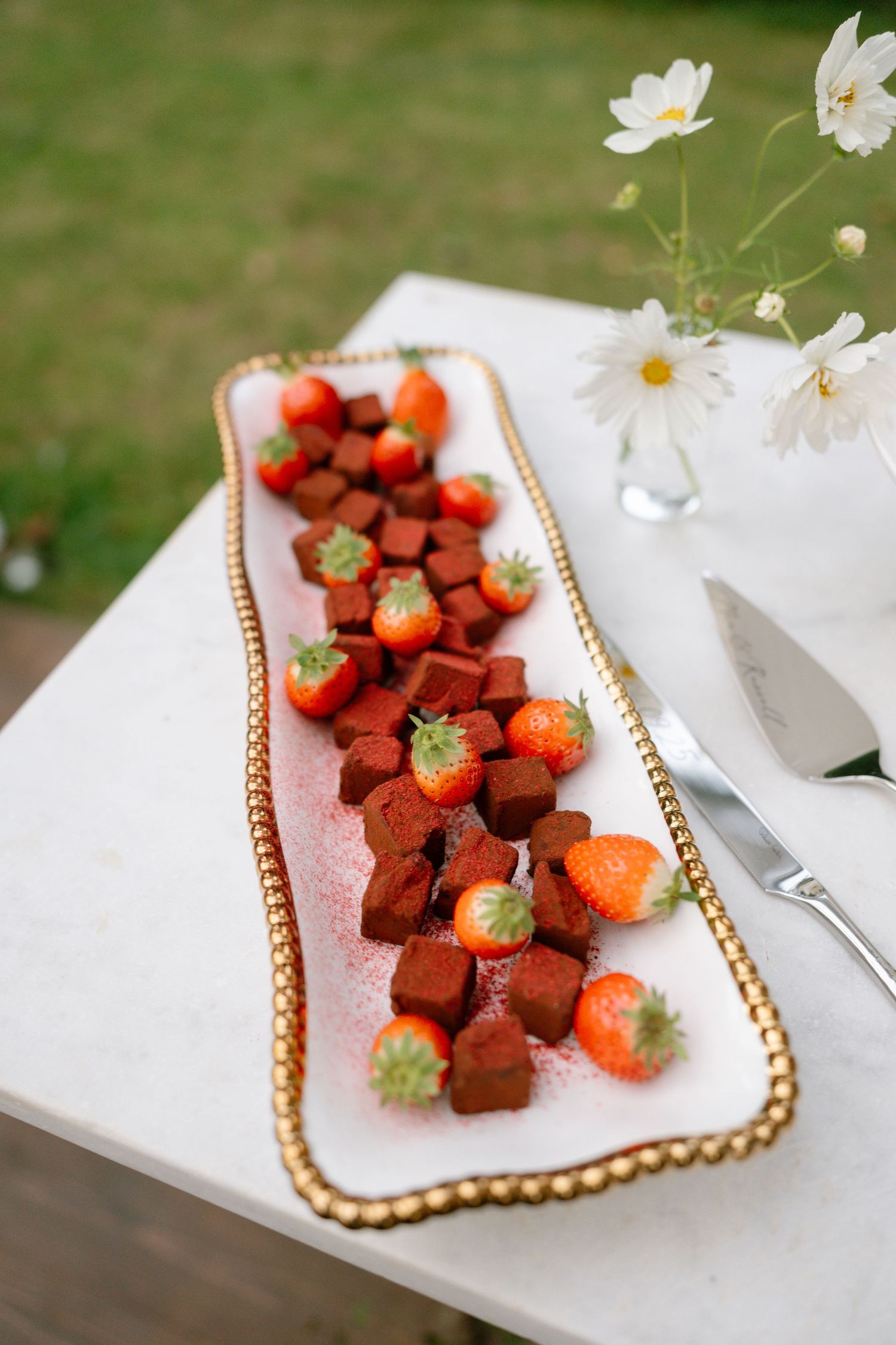 Fresh strawberries and chocolate truffles displayed on an elegant gold-rimmed white platter.