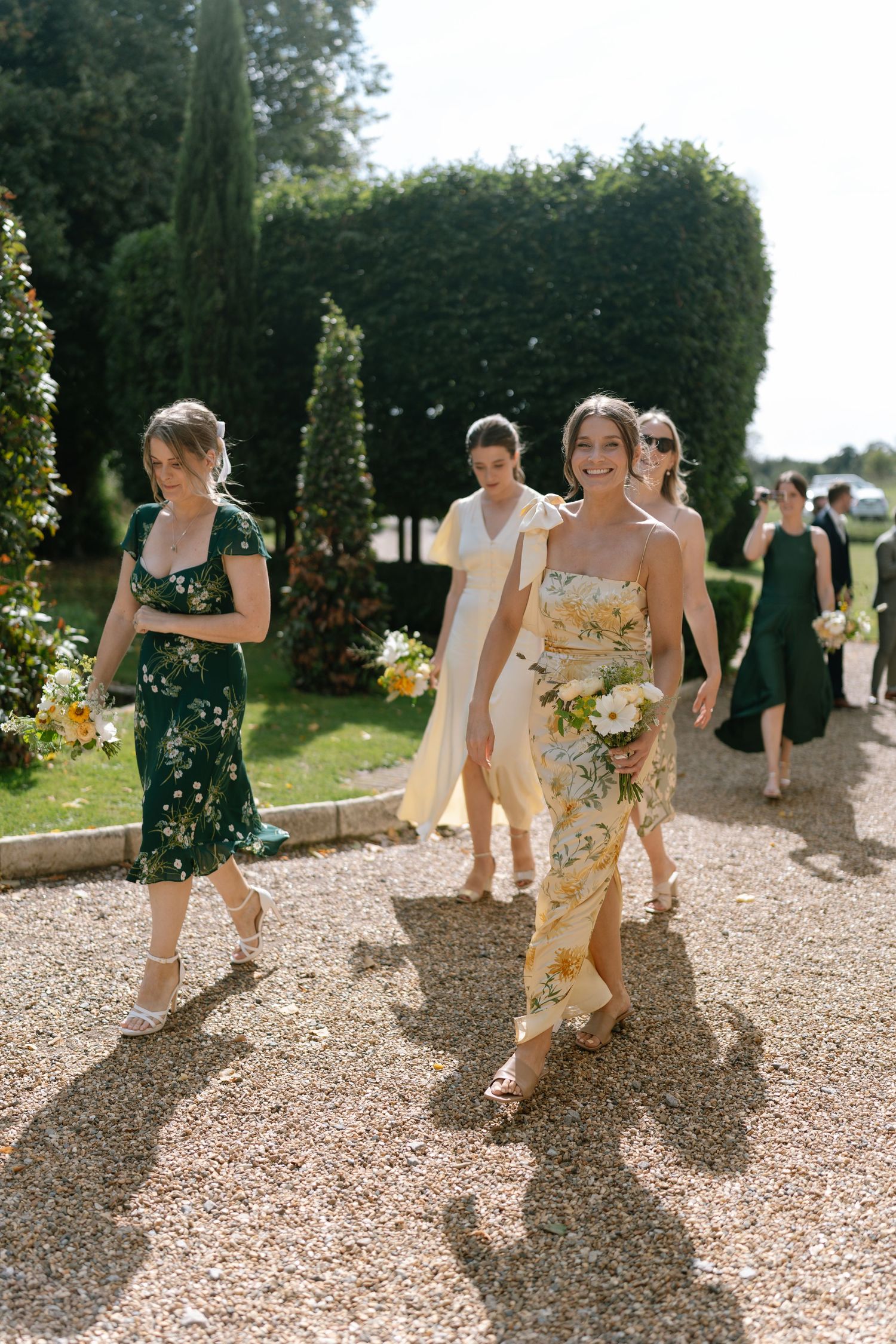 Wedding party walking along a gravel path in a garden setting.