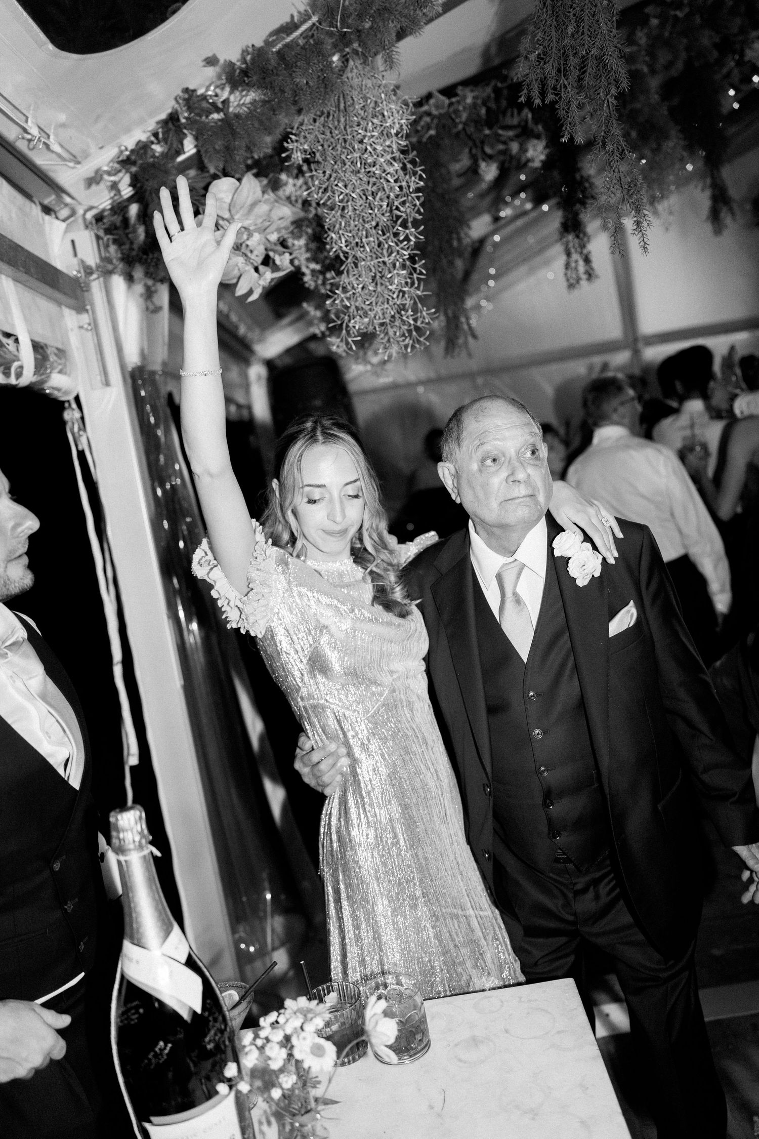 Wedding guests dance and celebrate under decorative greenery at an indoor reception.