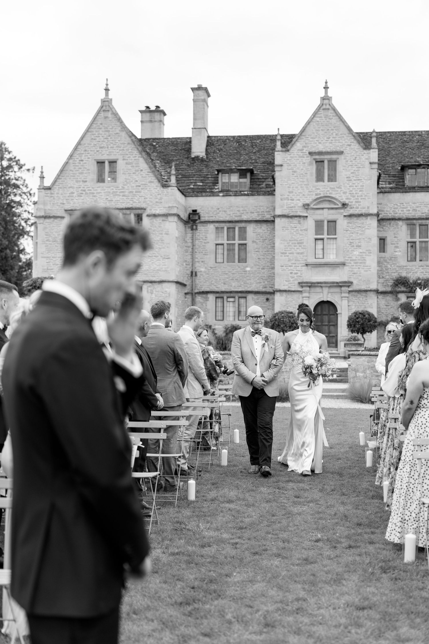 Bride walking down outdoor aisle with escort at English manor house wedding ceremony.
