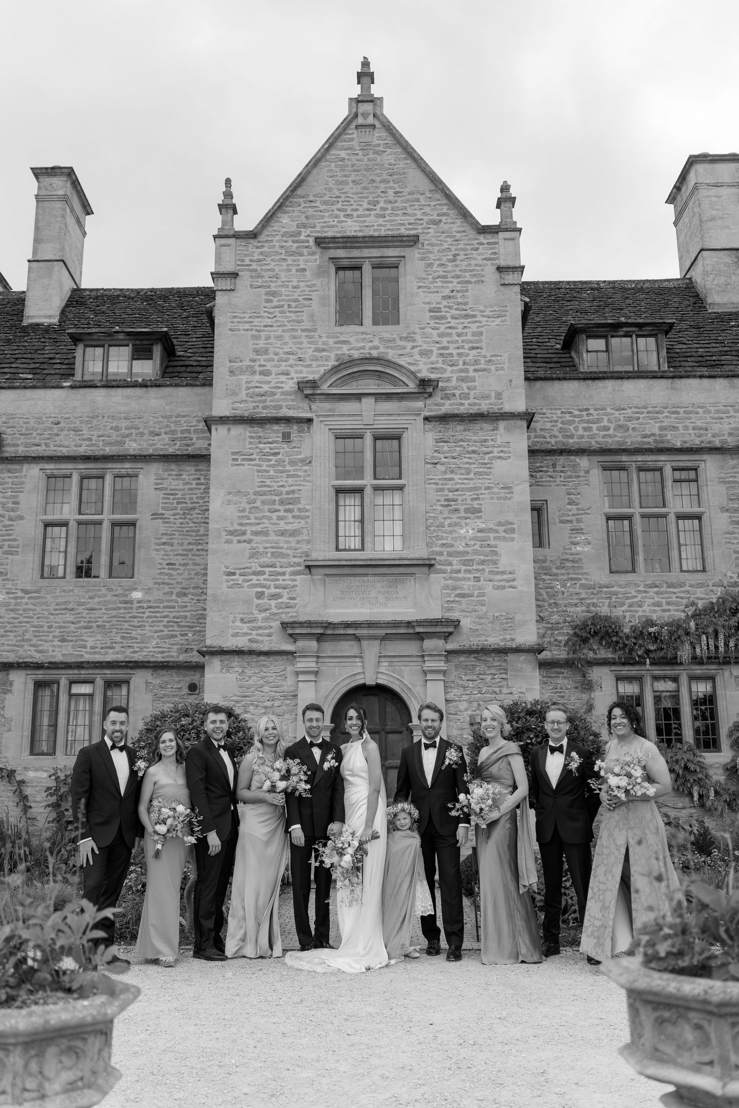 Black and white wedding party portrait in front of grand historic stone manor house wedding venue.