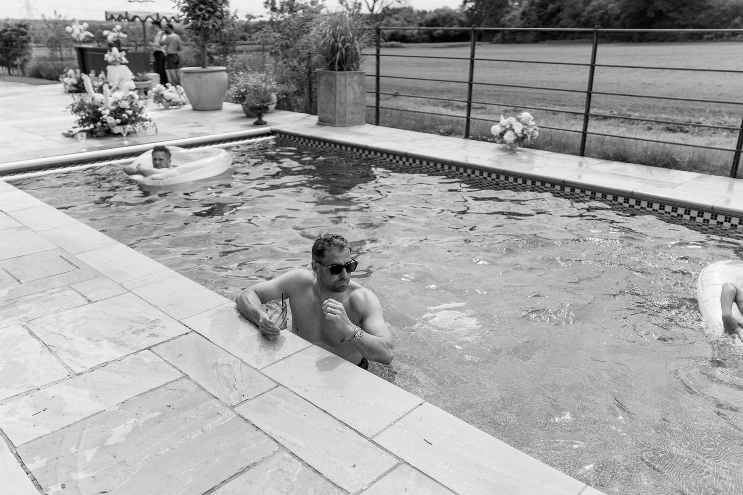 Wedding guests swimming and relaxing in an outdoor pool at a countryside wedding celebration.