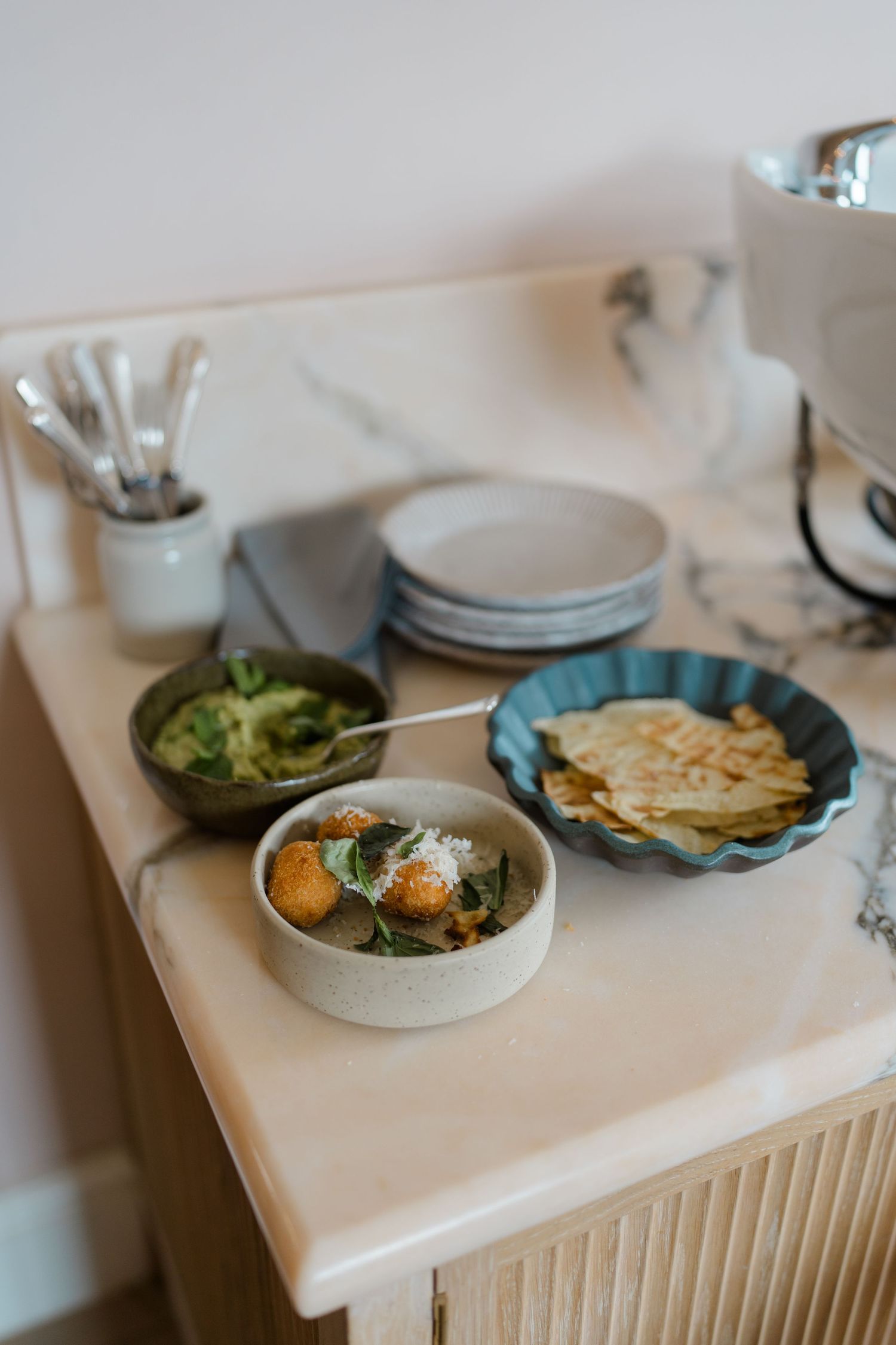 A buffet spread with guacamole, flatbread, and a curry dish on a marble countertop.
