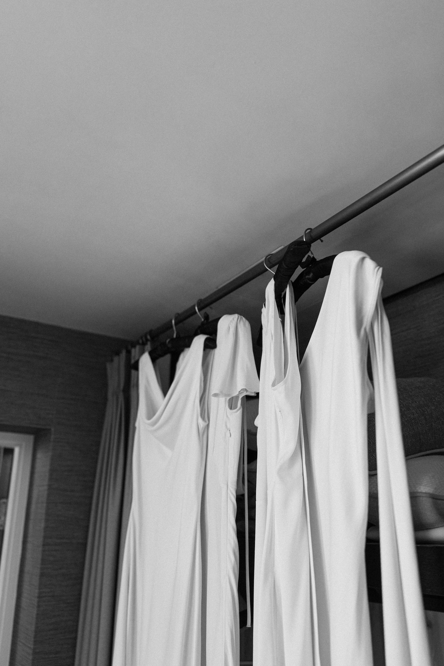White bridesmaid dresses hanging on a rod in black and white wedding preparation photo.
