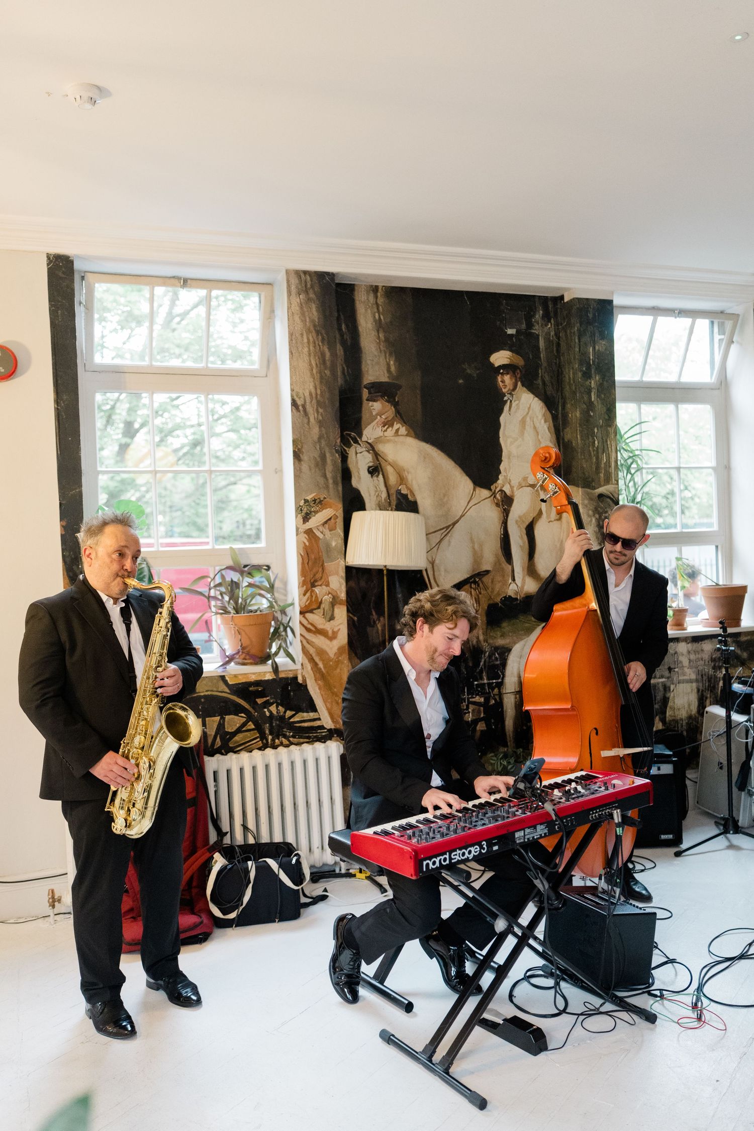 Jazz trio performing with saxophone, keyboard, and double bass in a bright white room at a wedding.