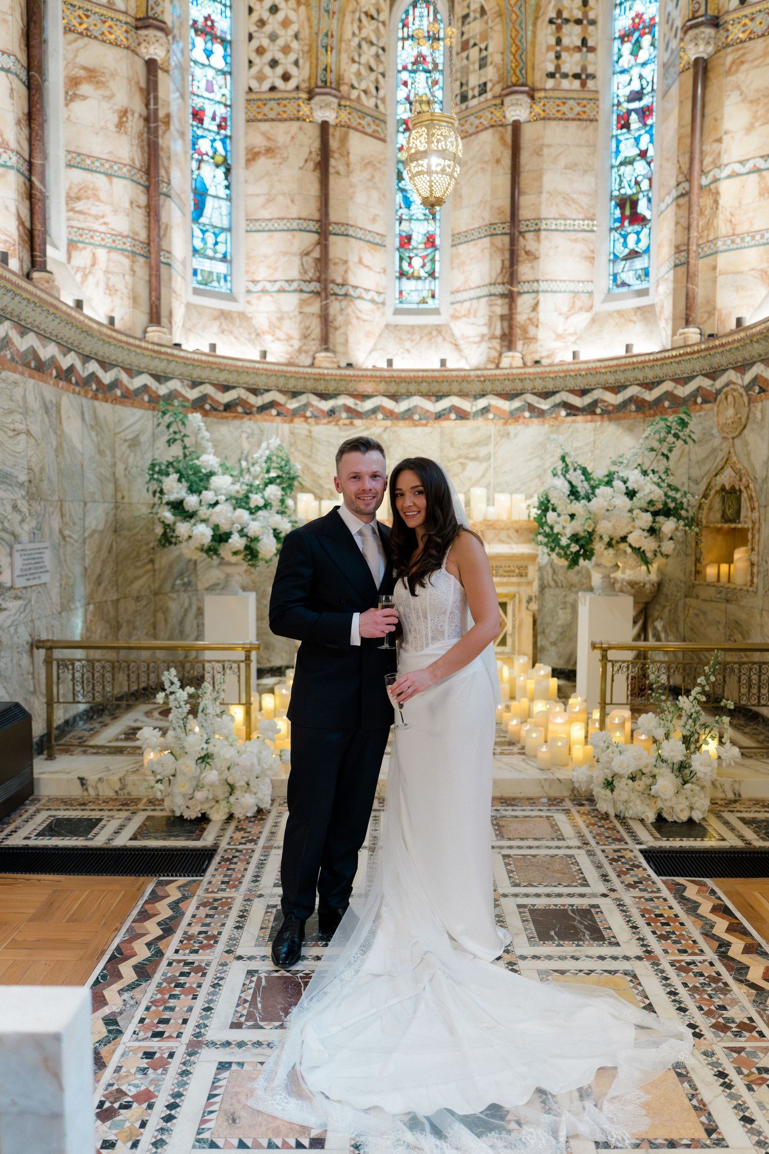 Bride and groom portrait in breathtaking chapel surrounded by white floral arrangements and candles.