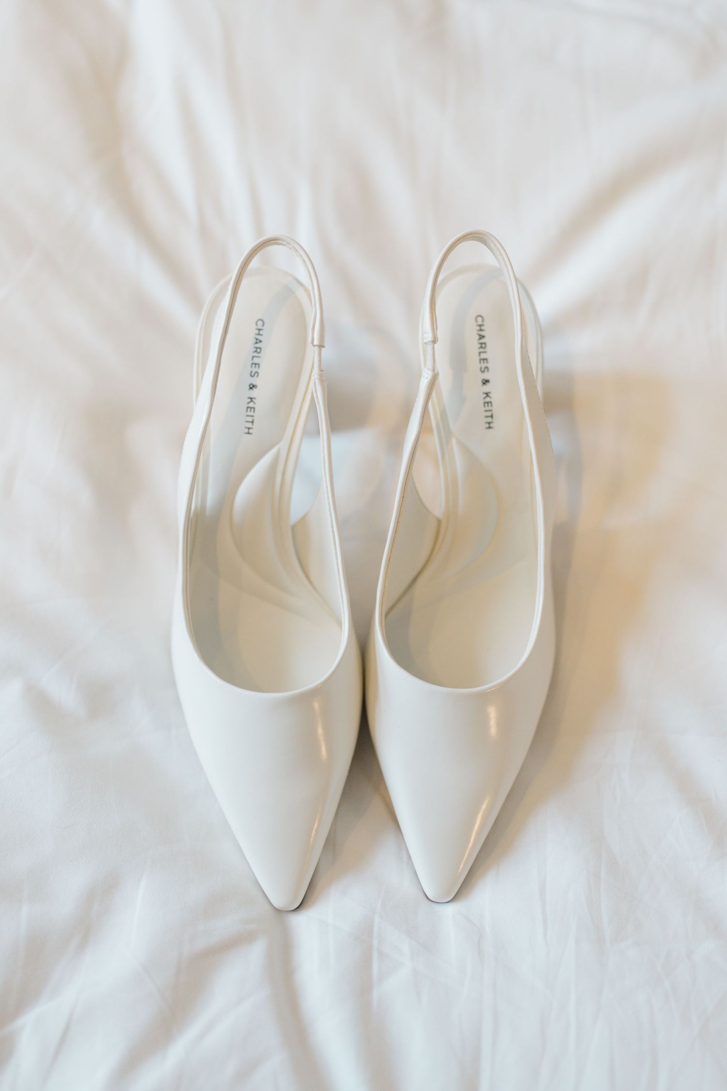 White Charles & Keith pointed-toe slingback heels on white fabric background.