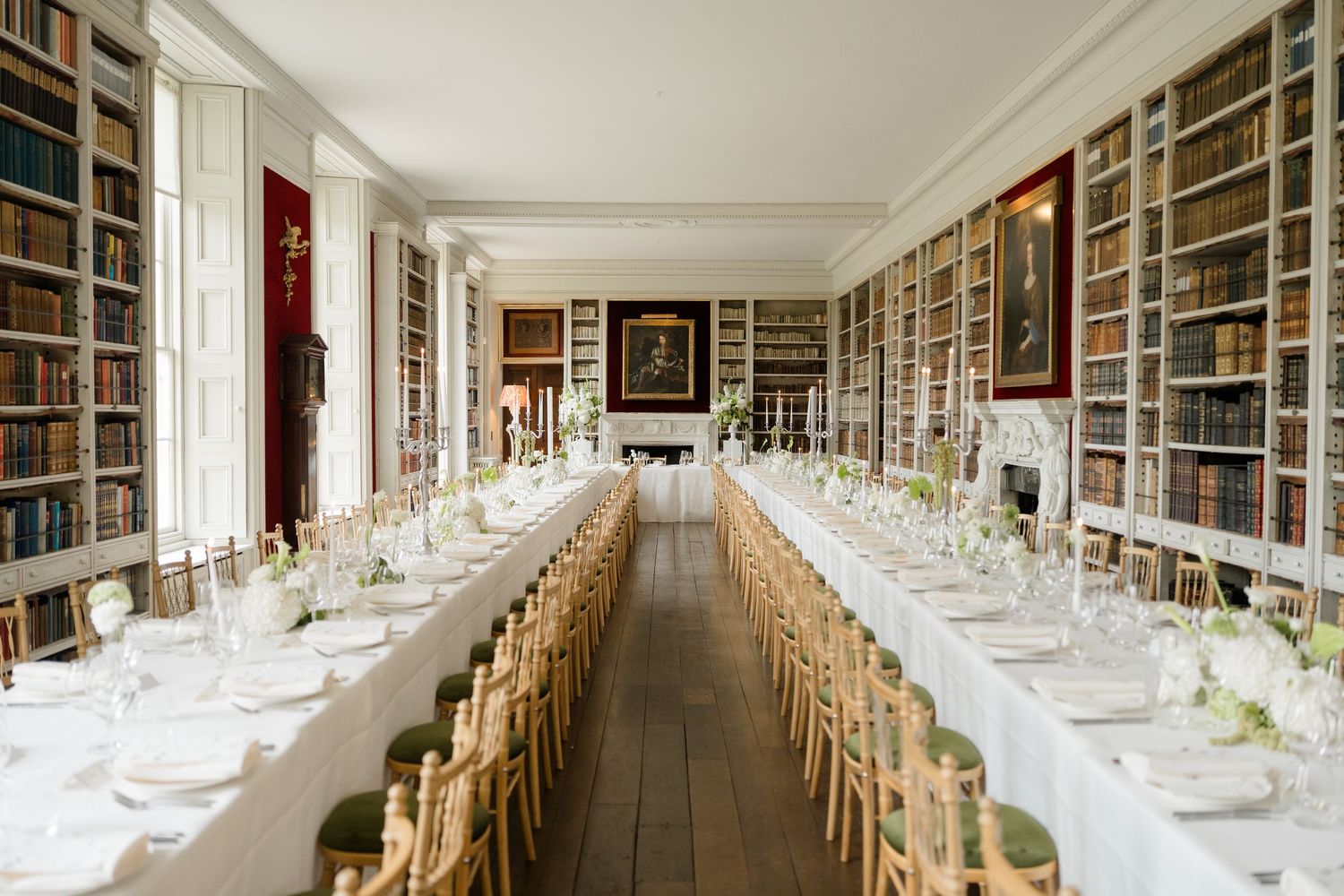 Elegant wedding reception in a library venue with long white tables set between floor-to-ceiling bookshelves.