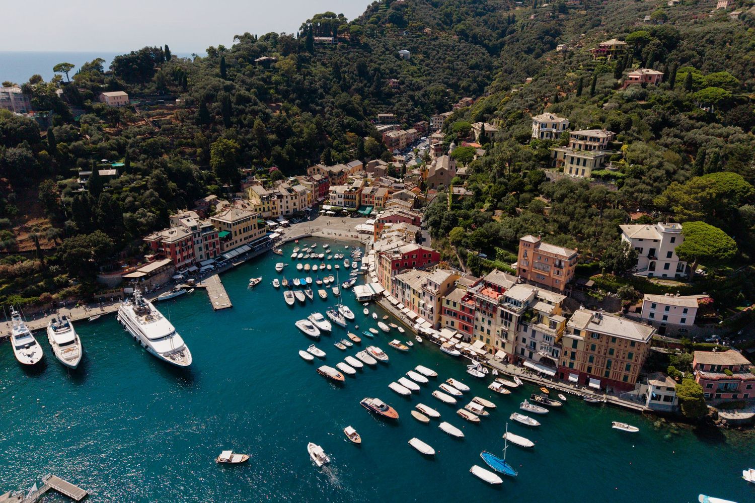 Aerial view of Portofino harbor with colorful buildings, boats, and turquoise Mediterranean waters.