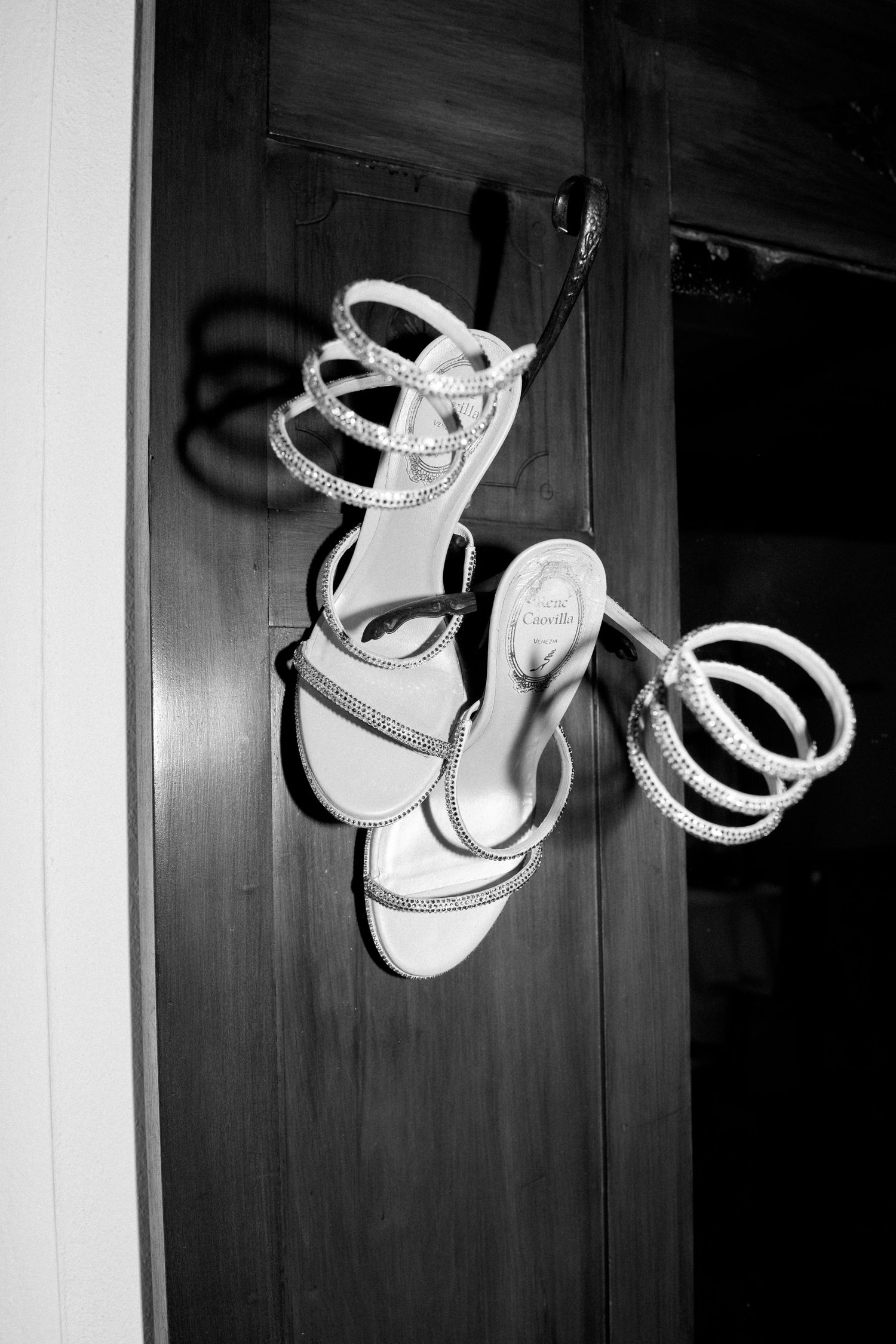 White strappy wedding shoes photographed in black and white against a wooden background.