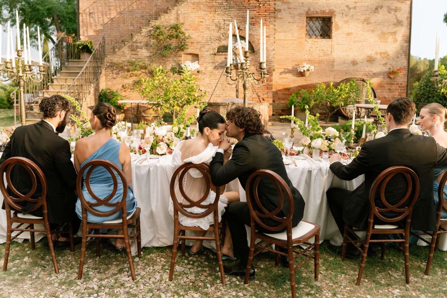 Long dining table setup against rustic stone wall for outdoor wedding reception.
