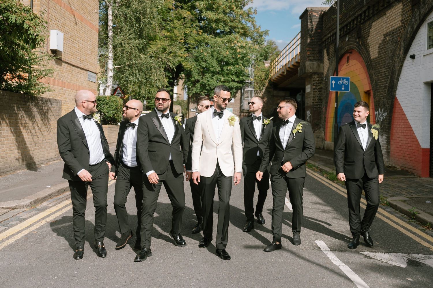 Group in formal black and white attire walking along a brick-lined street.