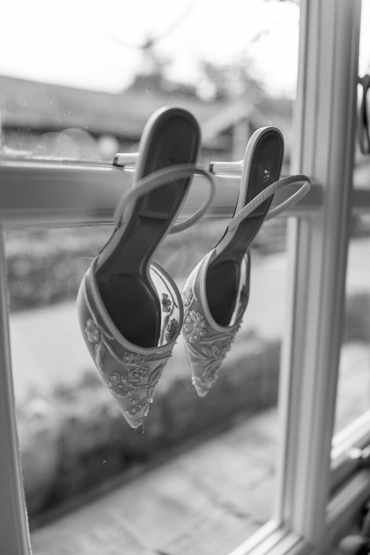 Black and white photo of ornate wedding shoes perched on a windowsill.