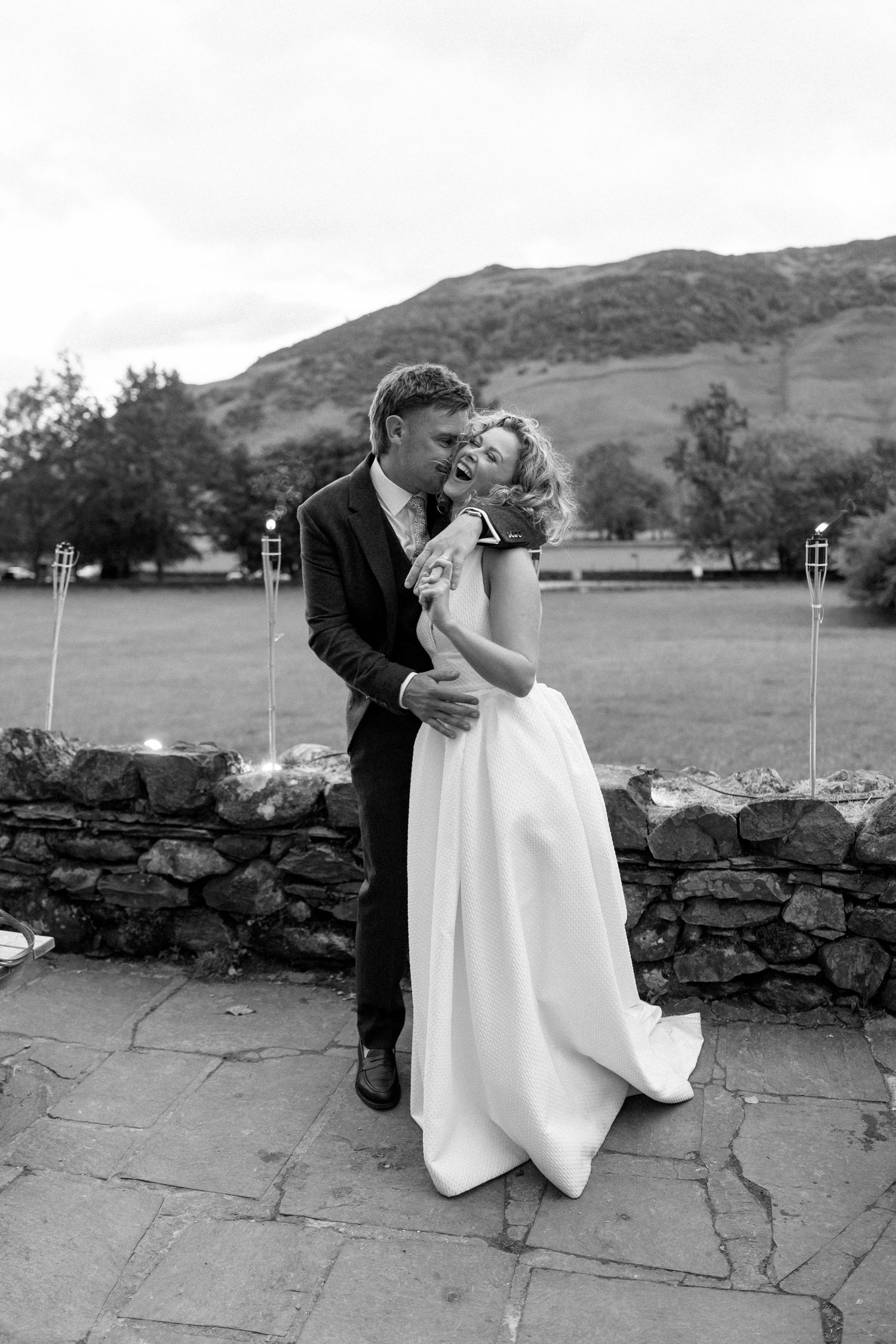 Romantic moment between newlyweds against rustic stone wall and mountain backdrop.