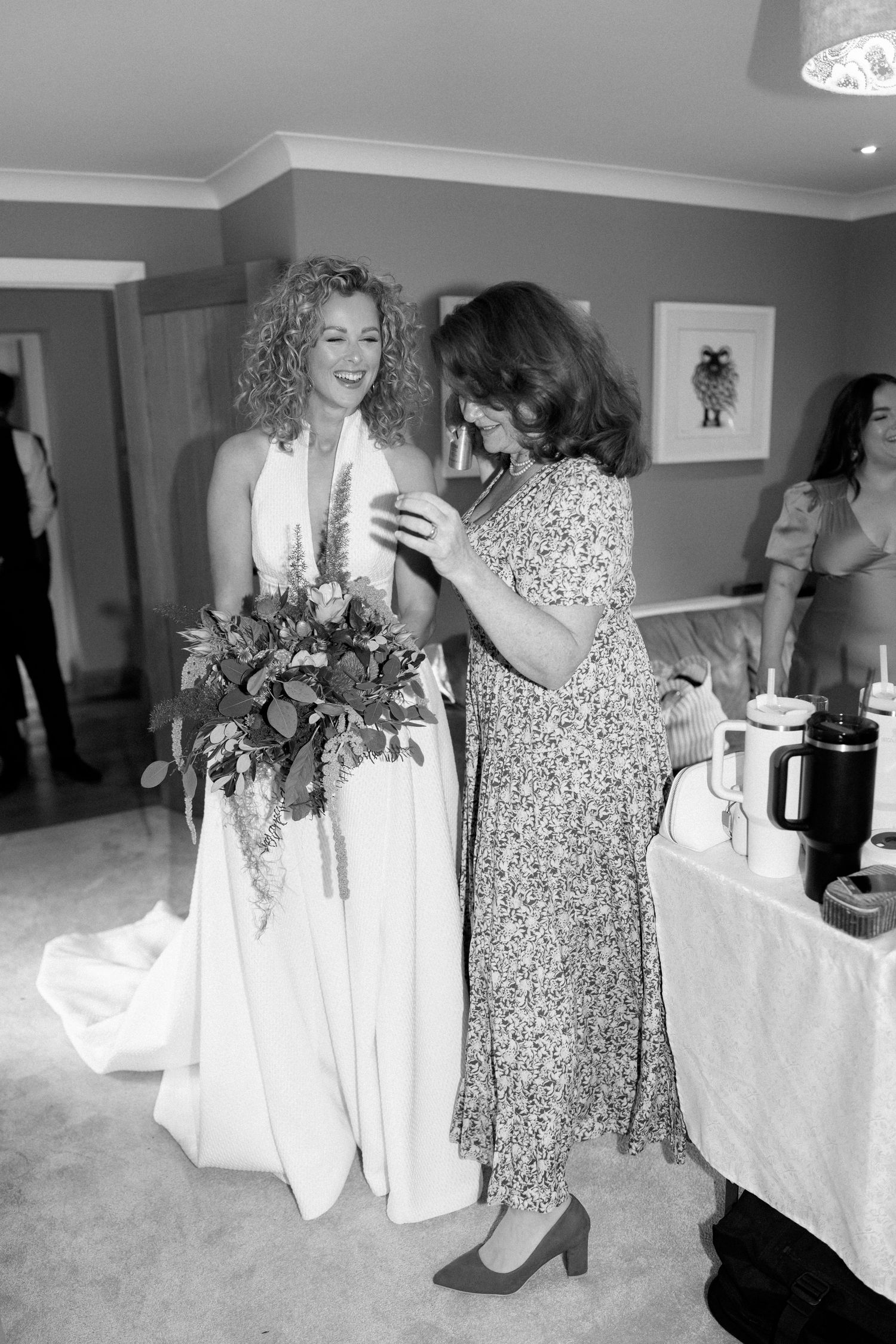 Wedding party members in white and floral dresses interact during pre-ceremony preparations.