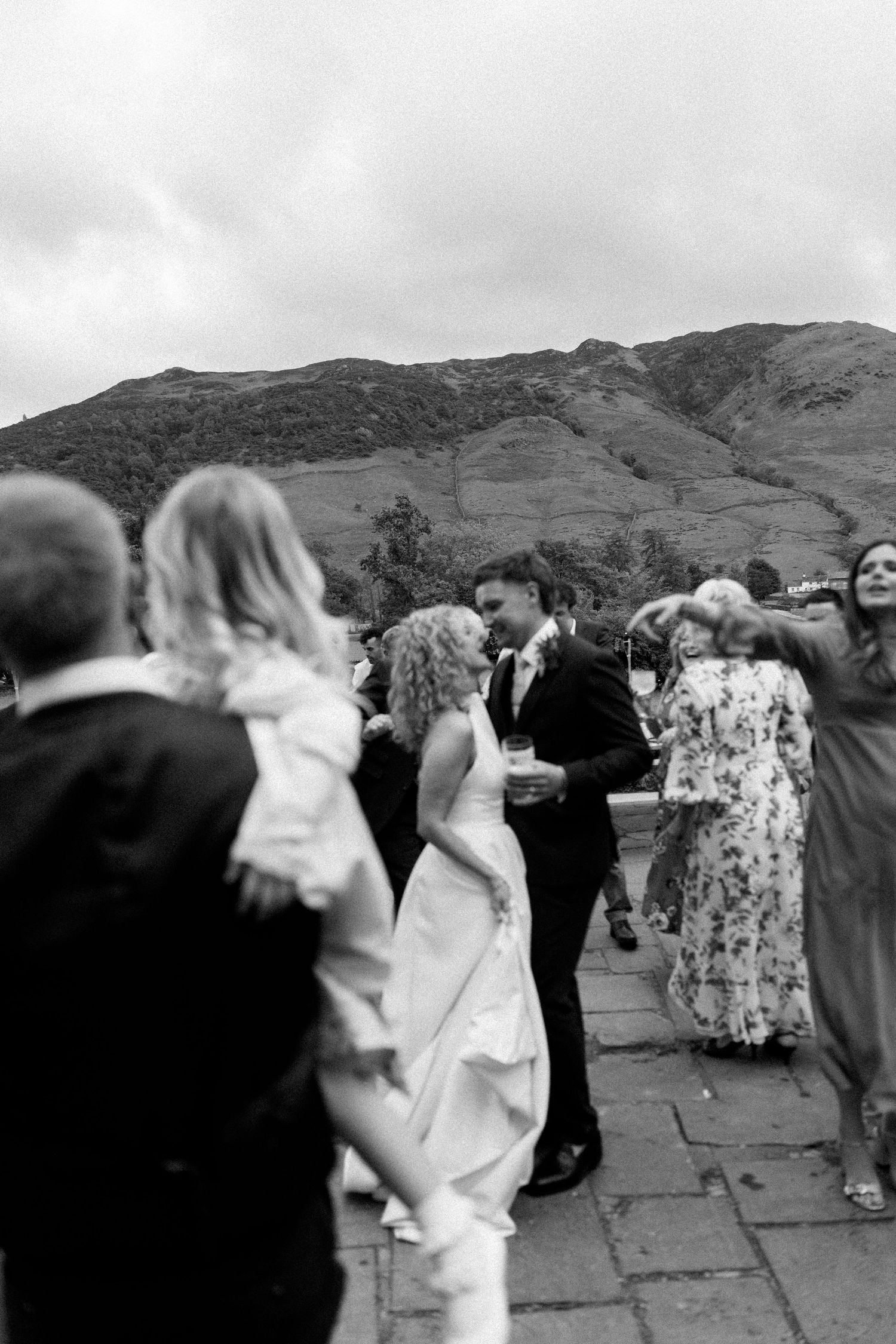 Wedding guests dance outdoors with dramatic mountain scenery in the background.