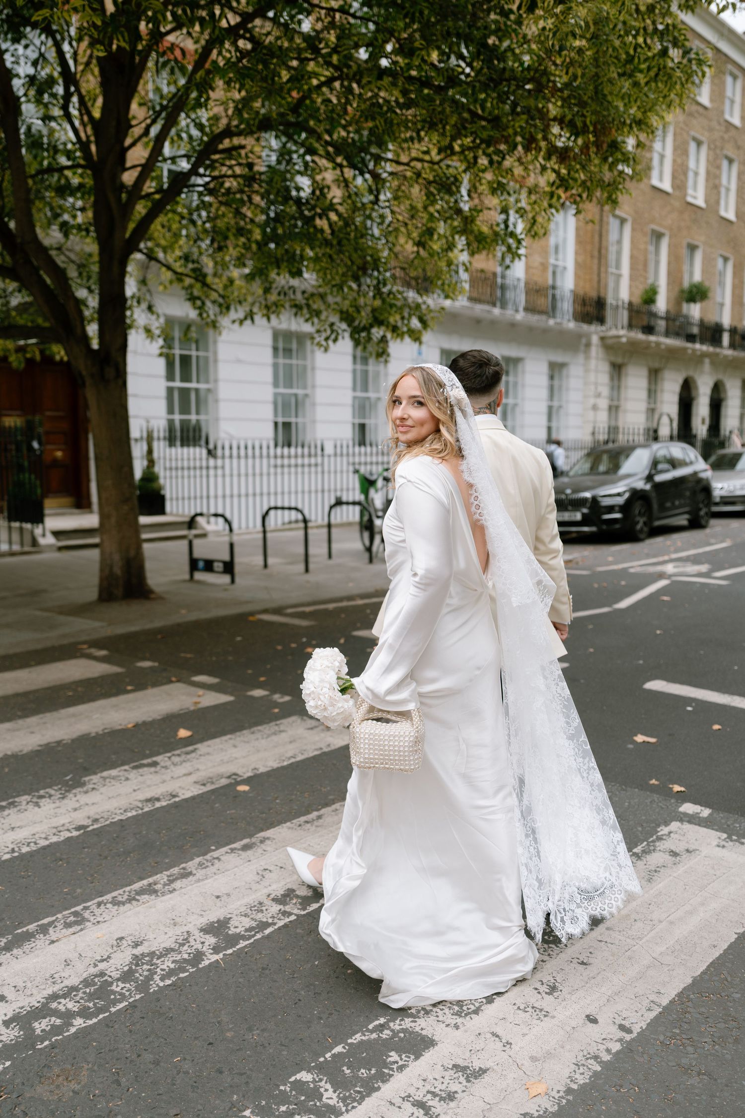 A bride in a flowing white dress and veil crosses a London street.