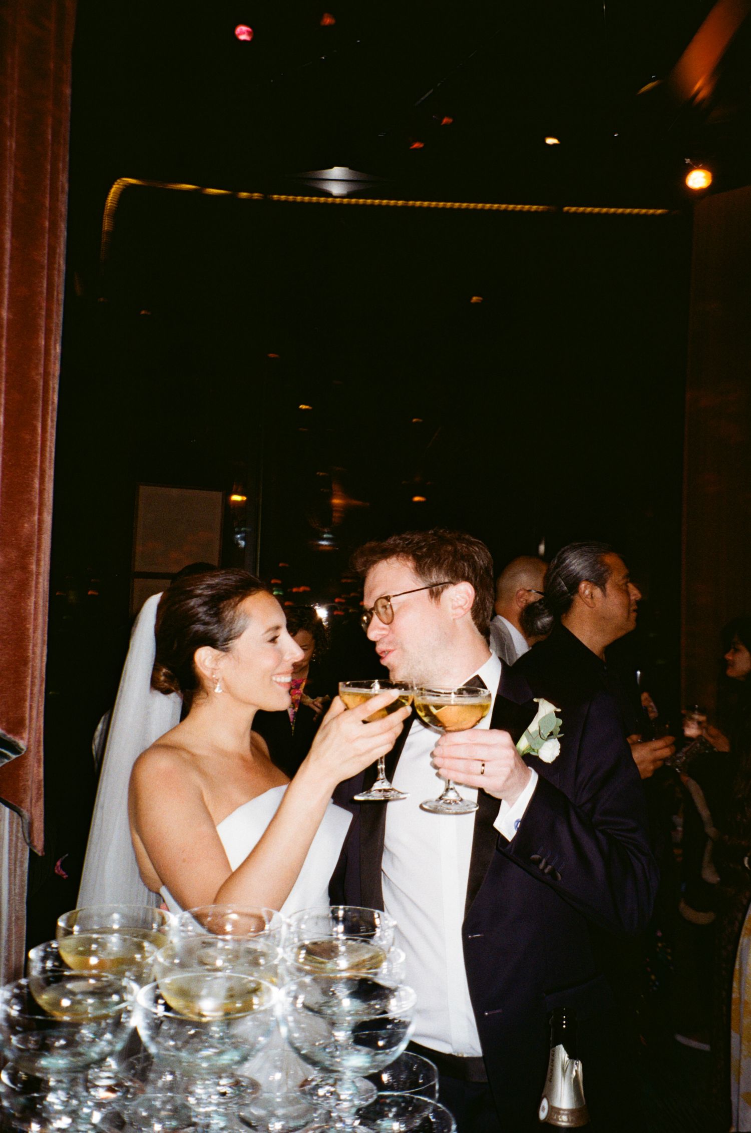 Wedding guests raise champagne glasses in a celebratory toast at a dimly lit reception.