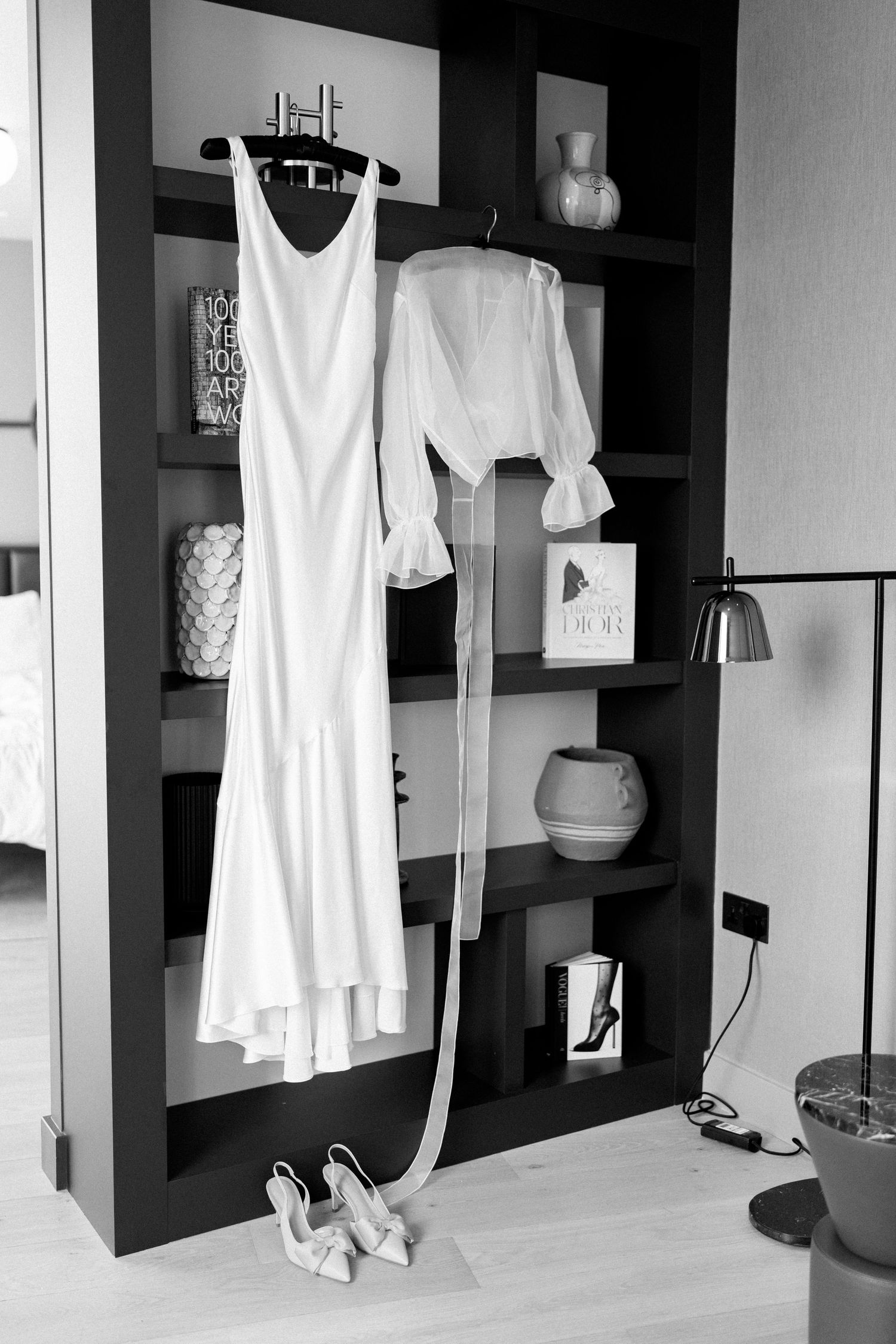 White wedding dress and blouse displayed on dark shelving unit with decorative items and shoes below.