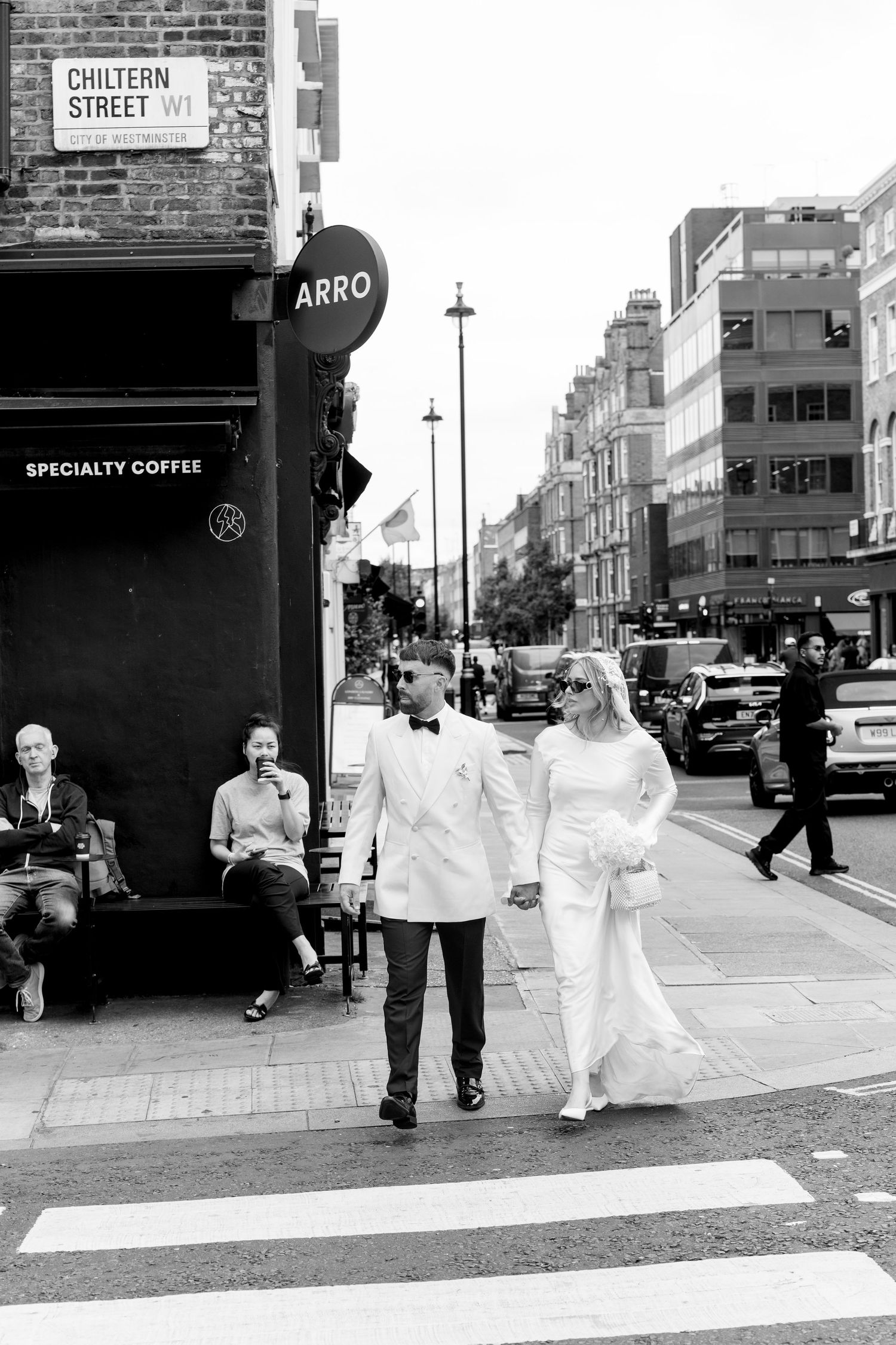 A couple in white wedding attire walks past Arro coffee shop on Whitfield Street in London.