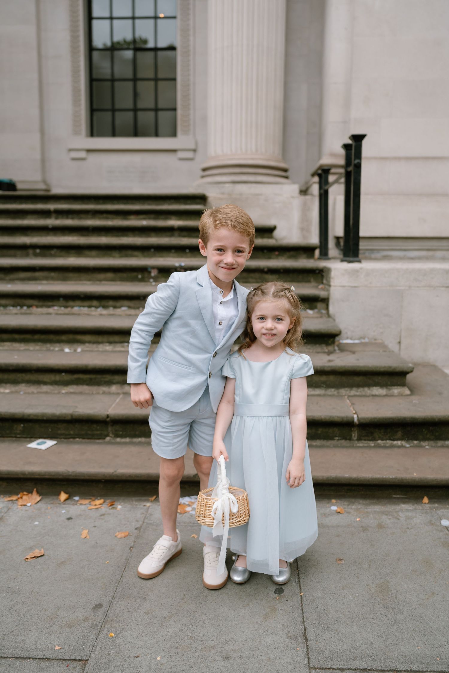 Two young children in light blue formal attire pose on stone steps.
