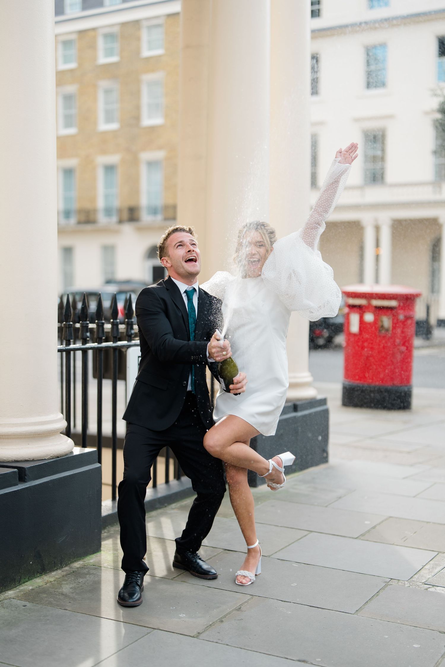 A playful couple dances and laughs together on a stone terrace with columns.