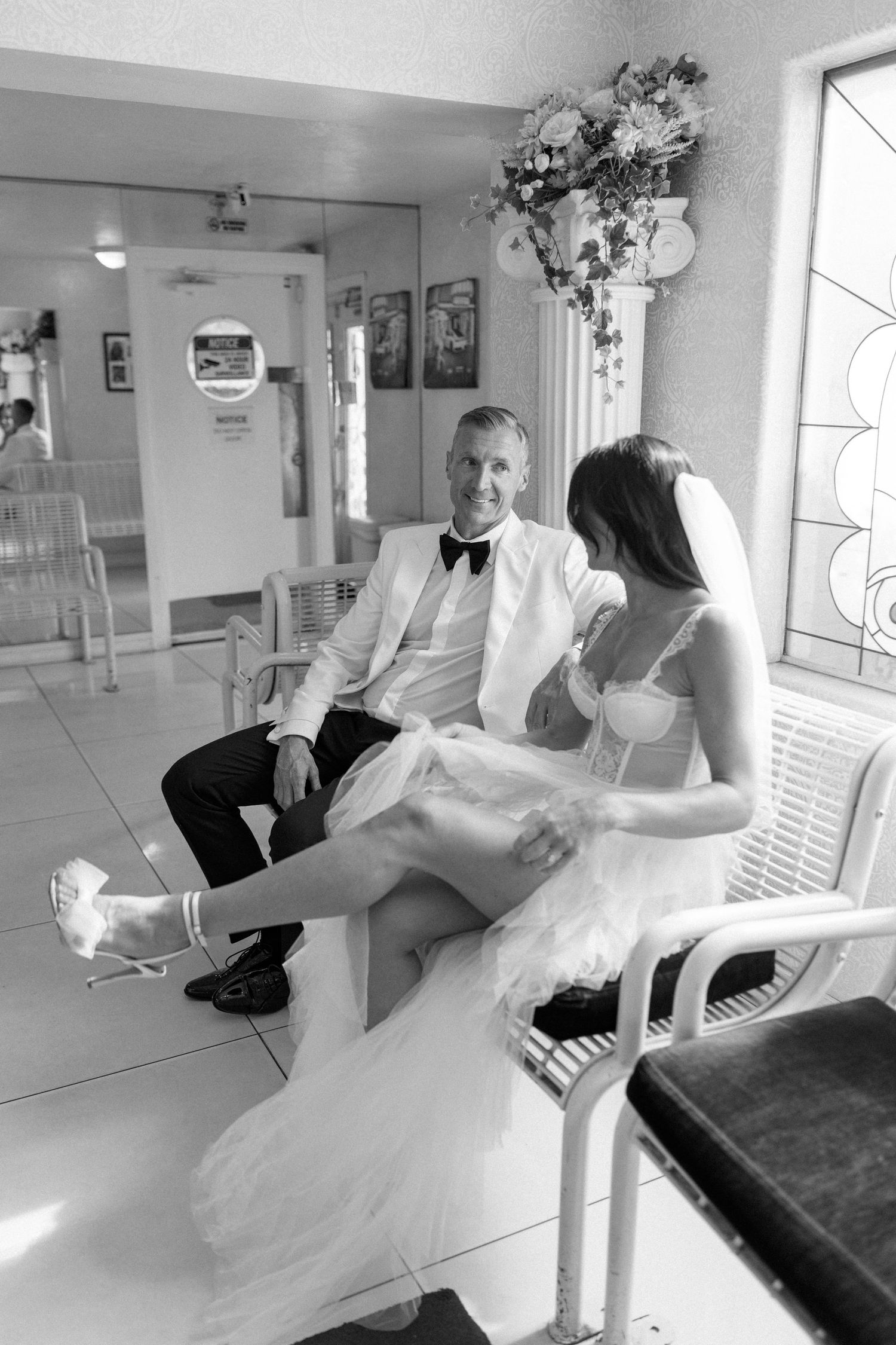 Black and white photos of couple sitting on white benches inside chapel.