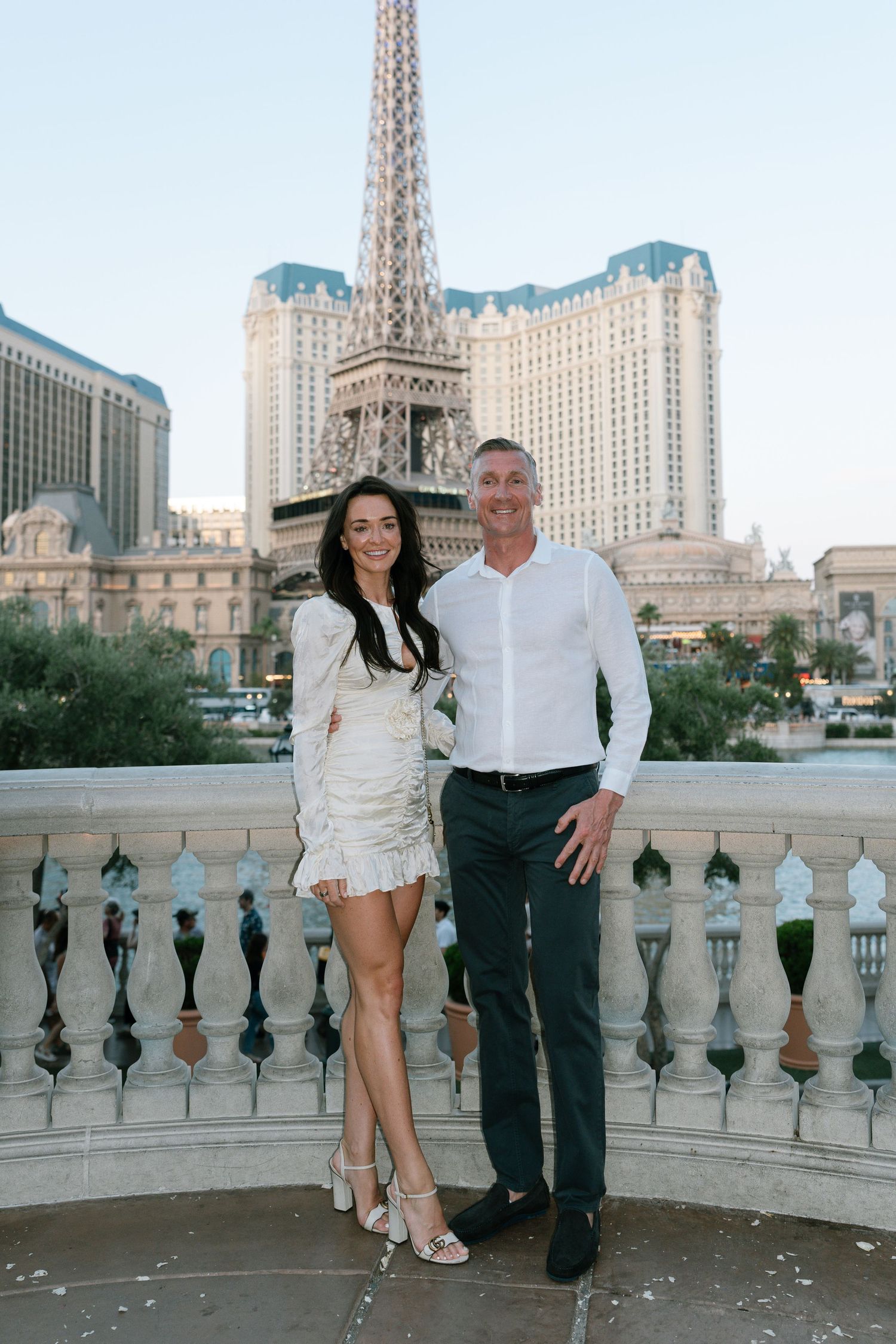 A couple poses on a balcony with the Paris Las Vegas hotel and Eiffel Tower replica in the background.