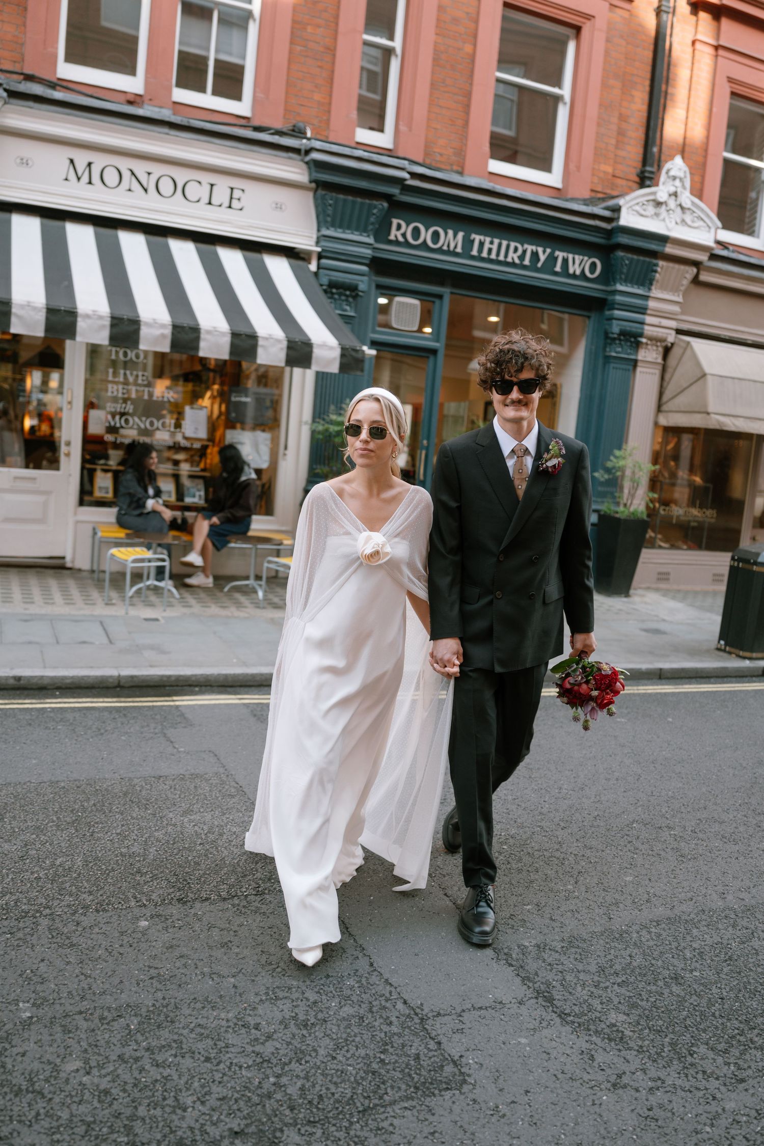 A couple walking past storefronts including Monocle and Room Thirty Two, with the bride in a flowing white dress.