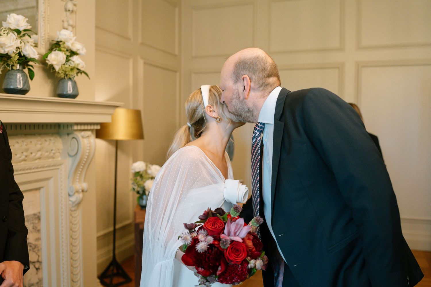 Couple exchanging vows in an elegant room with ornate white molding and a black fireplace.