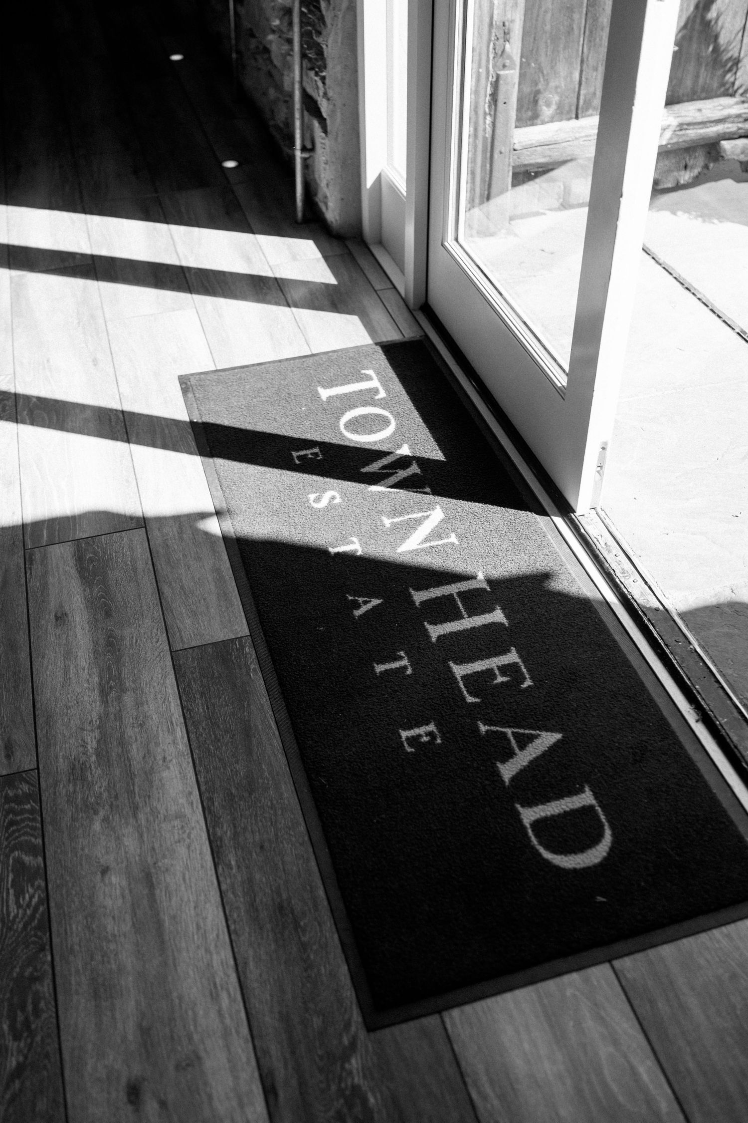 Black and white doormat with text casting shadows in sunlight.