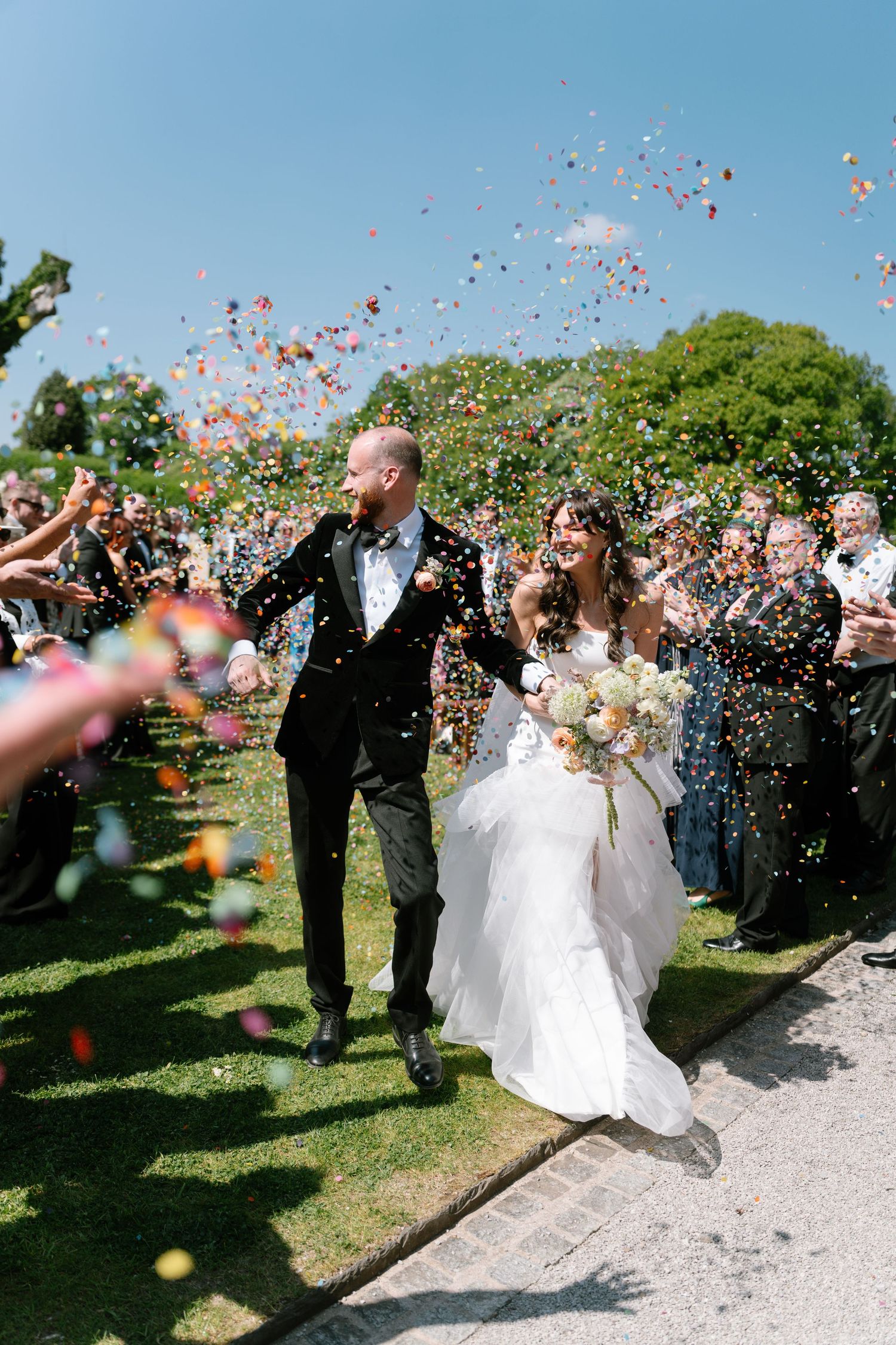 Colorful confetti fills the air as wedding guests celebrate on a beautiful garden path.