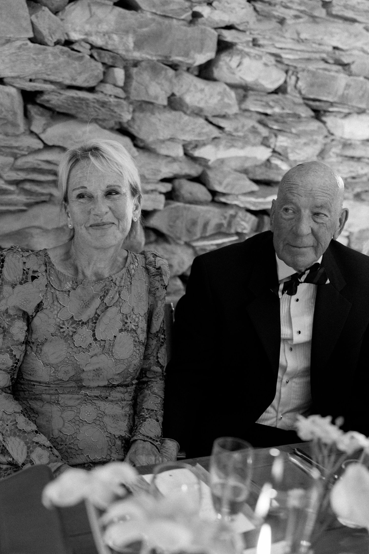 Elegant wedding reception with guests seated at formal dining tables against rustic stone walls.