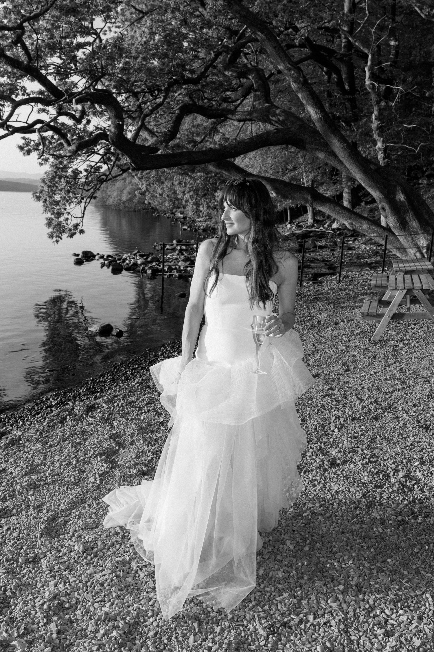 A white wedding dress flows elegantly against a natural outdoor backdrop with trees and grass.