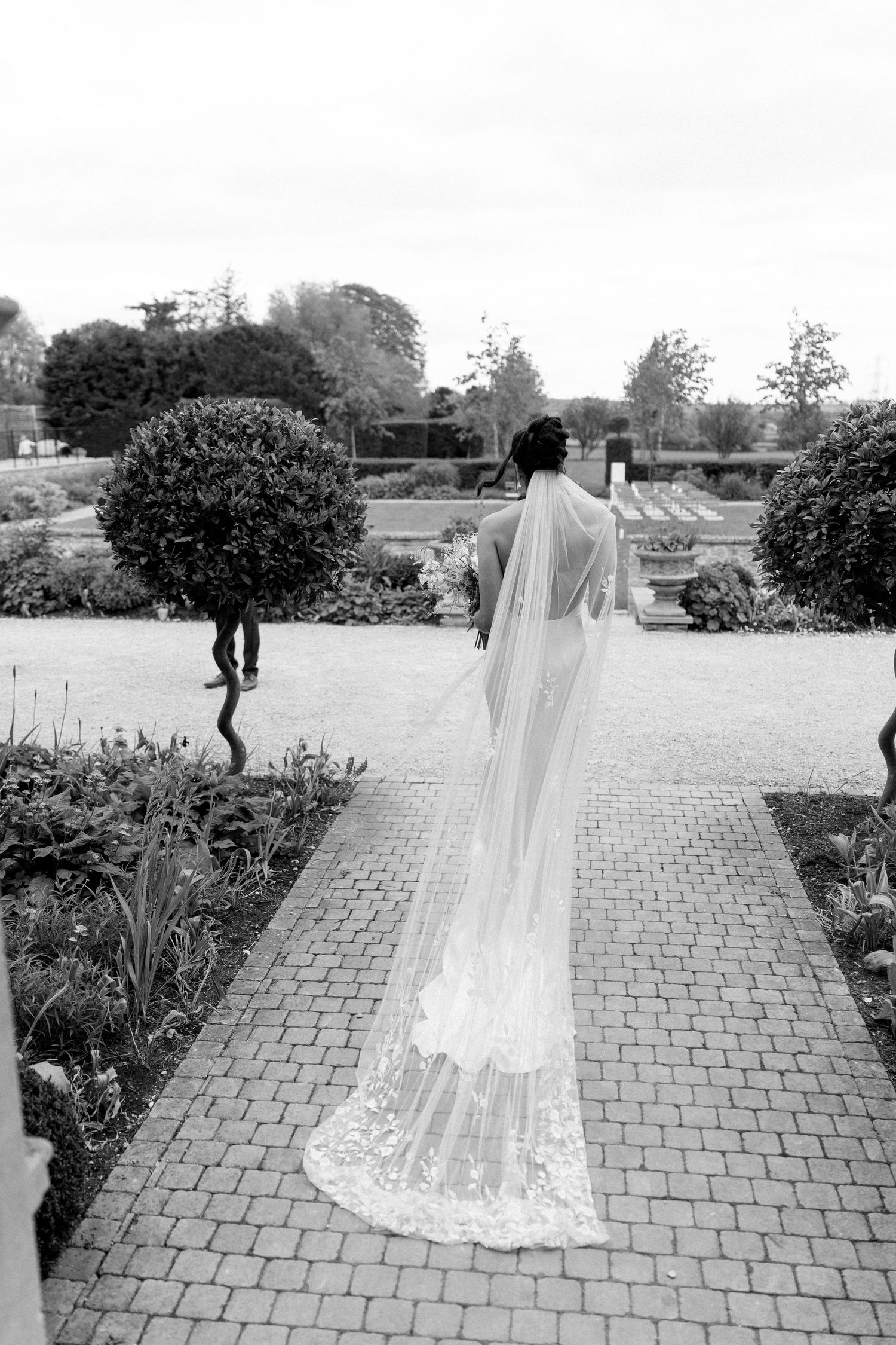 Bride in a halter wedding gown with a long lace cathedral veil walking through a formal garden.