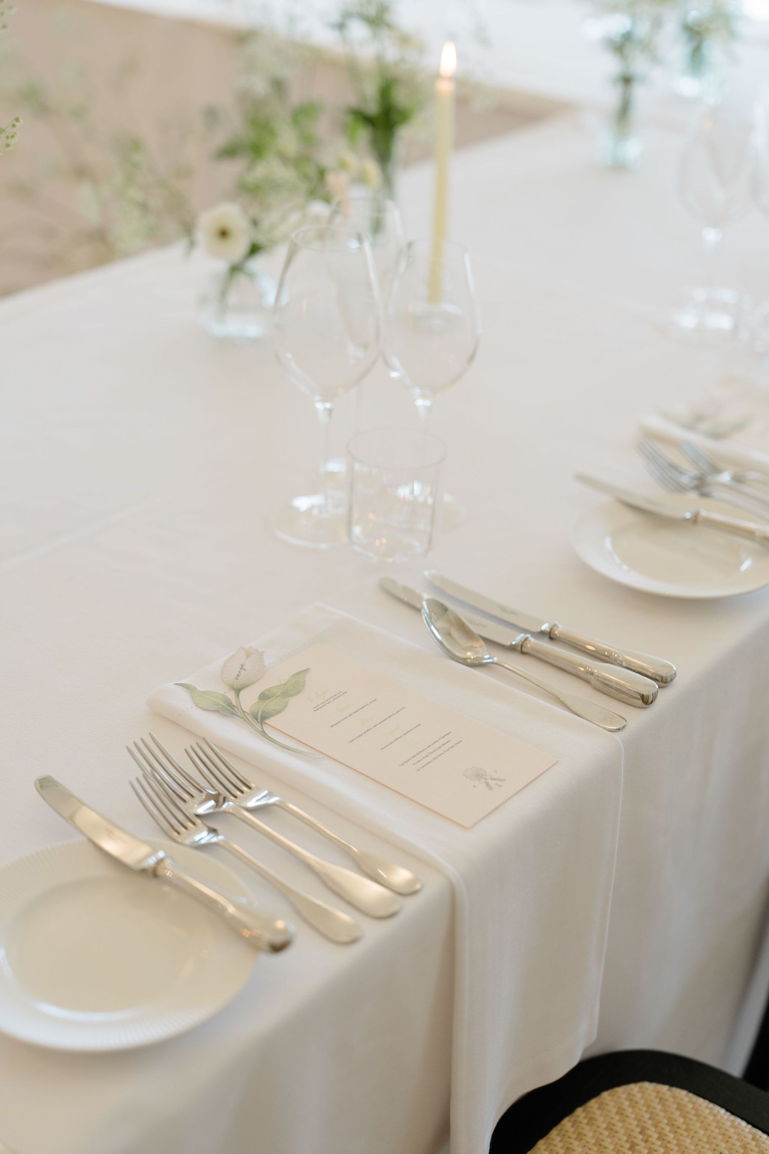 Elegant white wedding table setting with silver cutlery, crystal glasses, candles and cream menu cards.