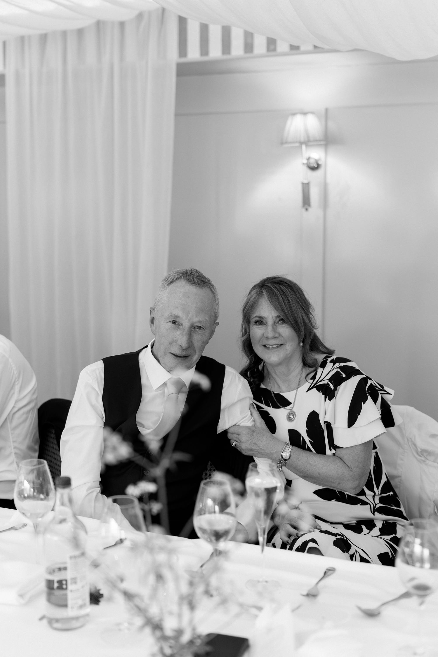 Black and white portrait of a smiling couple seated together at a wedding reception dinner table.