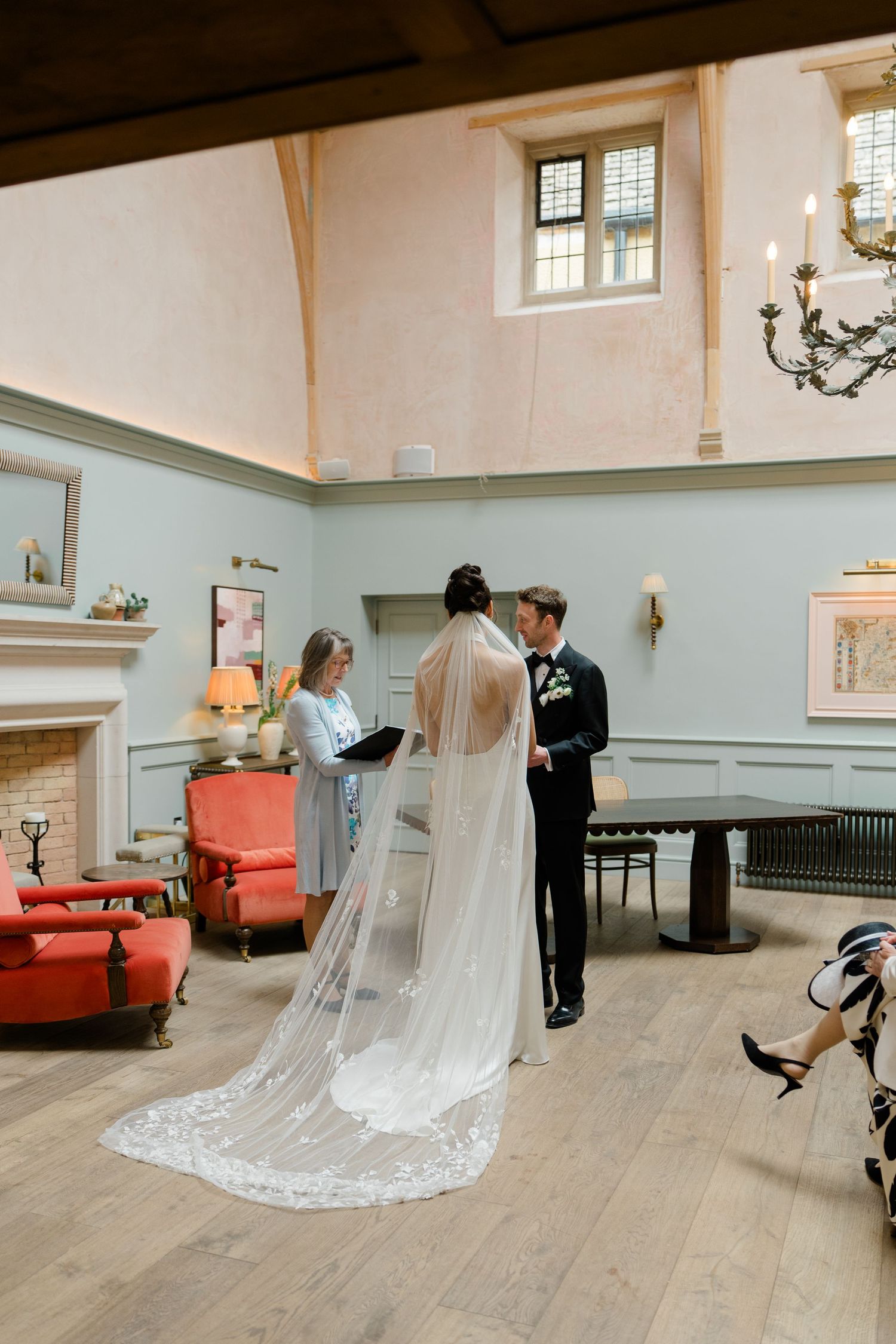 Bride in lace cathedral veil and groom exchange vows during intimate wedding ceremony in a charming manor house room.