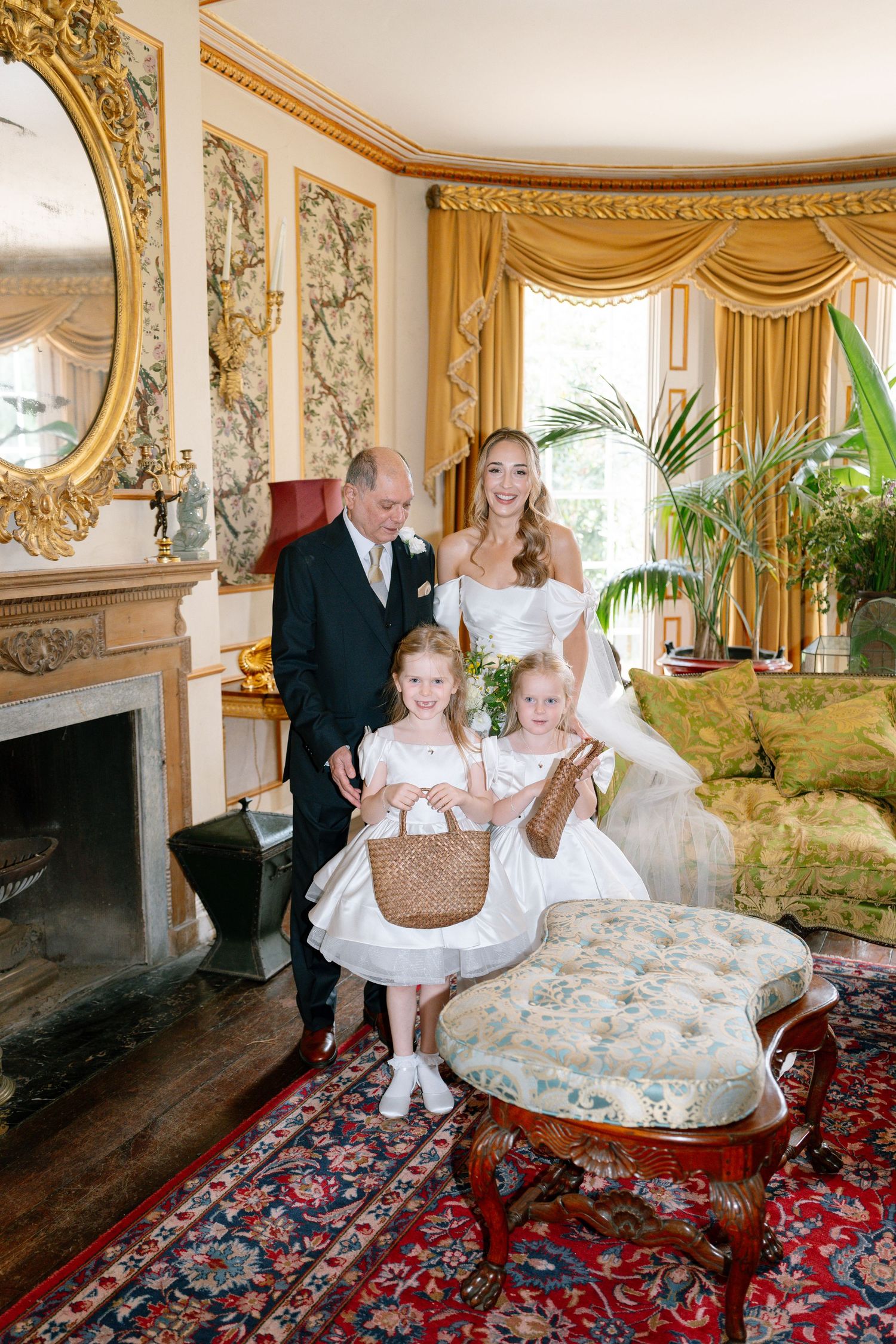 Wedding party gathers on an antique chaise lounge in an elegant room with gold trim.