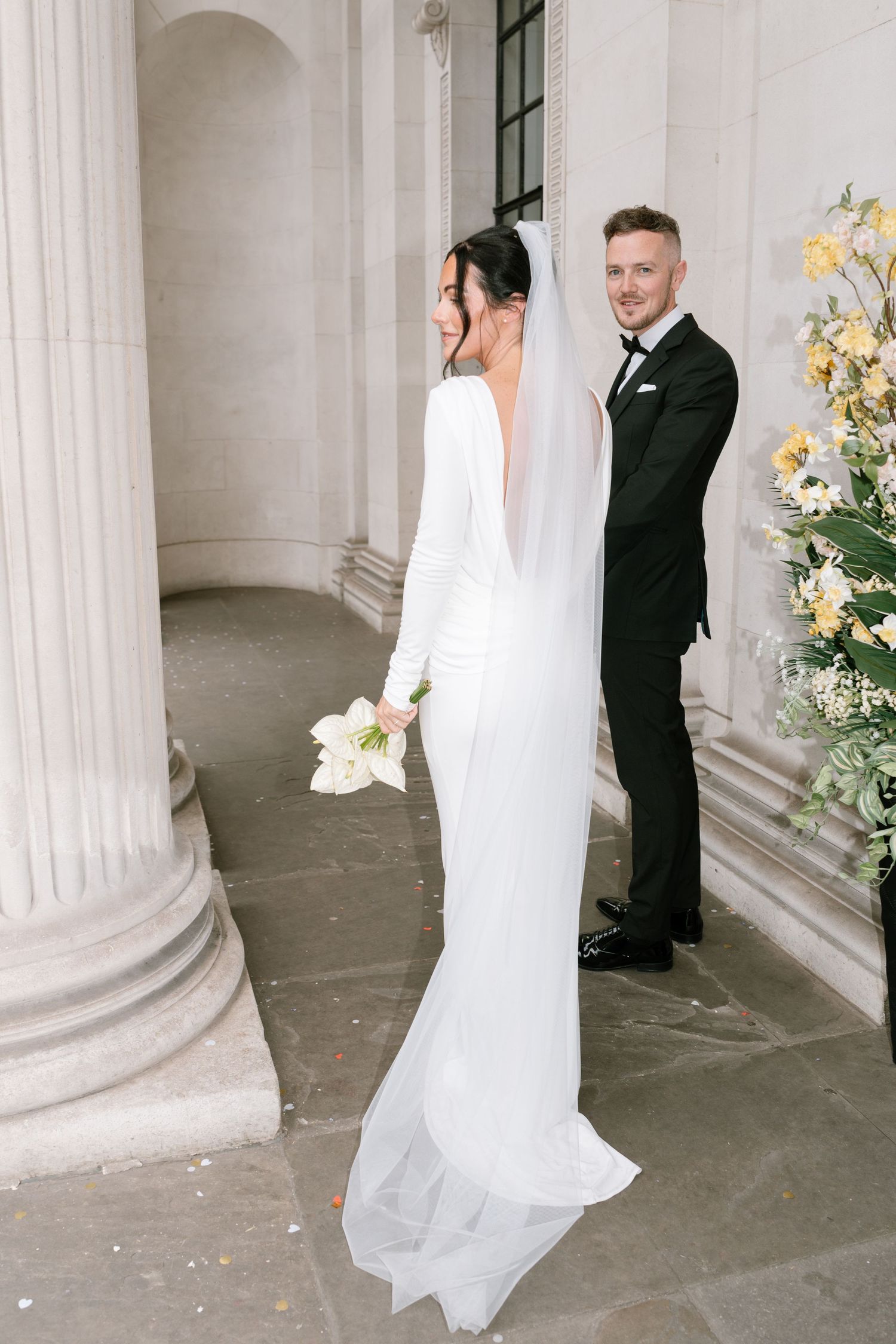 Elegant wedding scene with couple among classical columns and yellow floral arrangements.