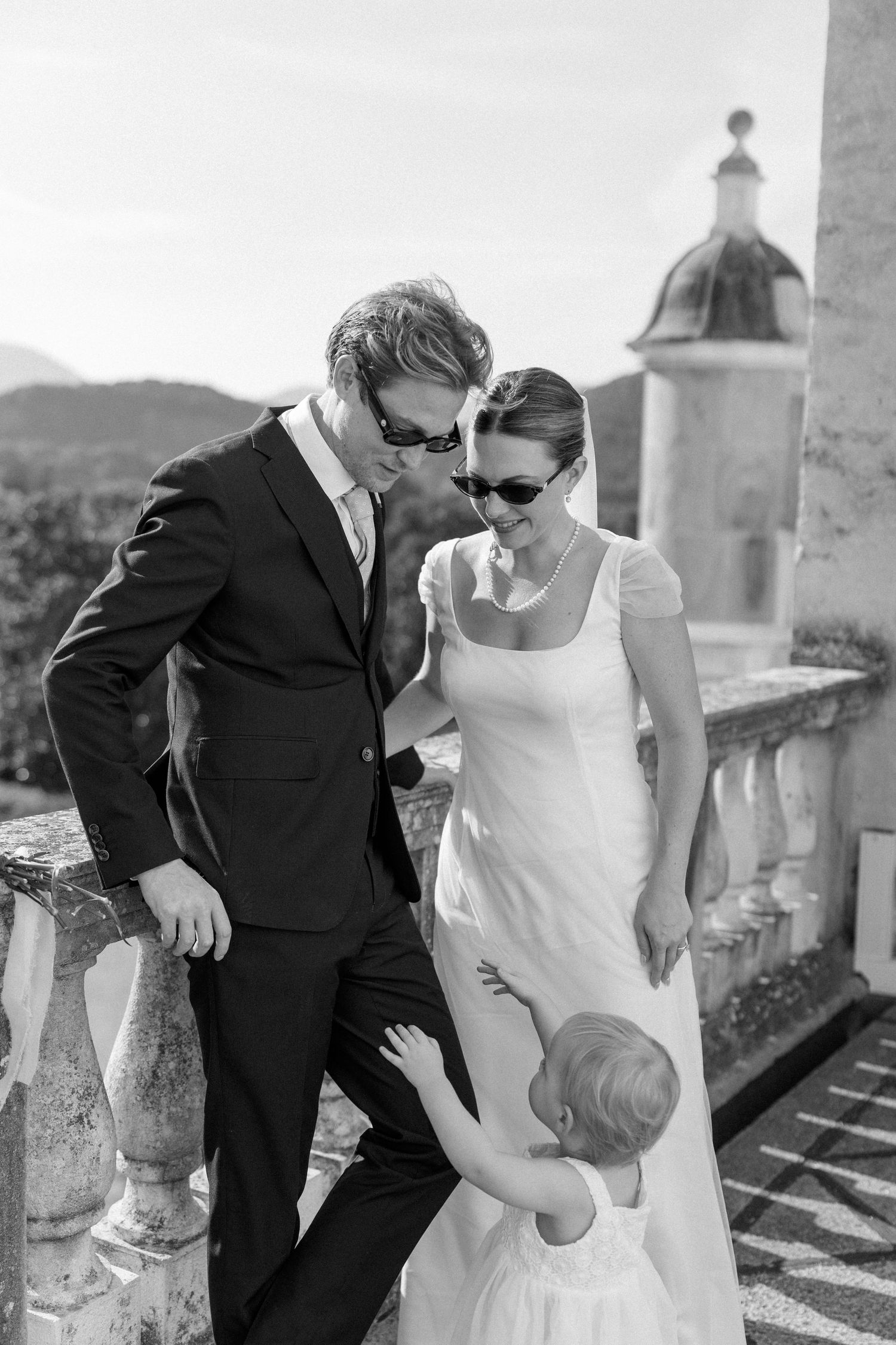 Black and white photo of wedding couple with small child on historic terrace.
