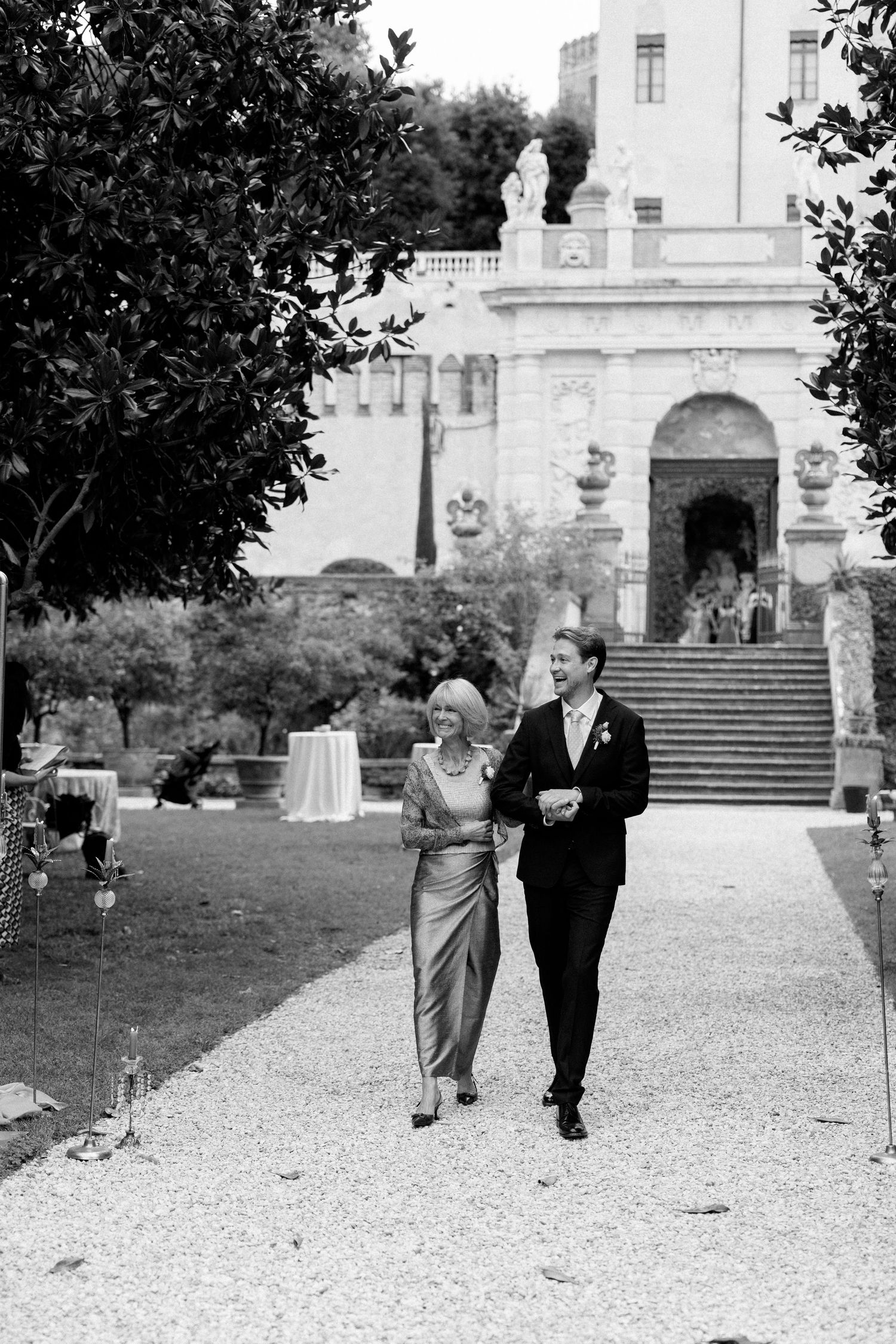 Couple strolling along a gravel path in front of a grand historic building.