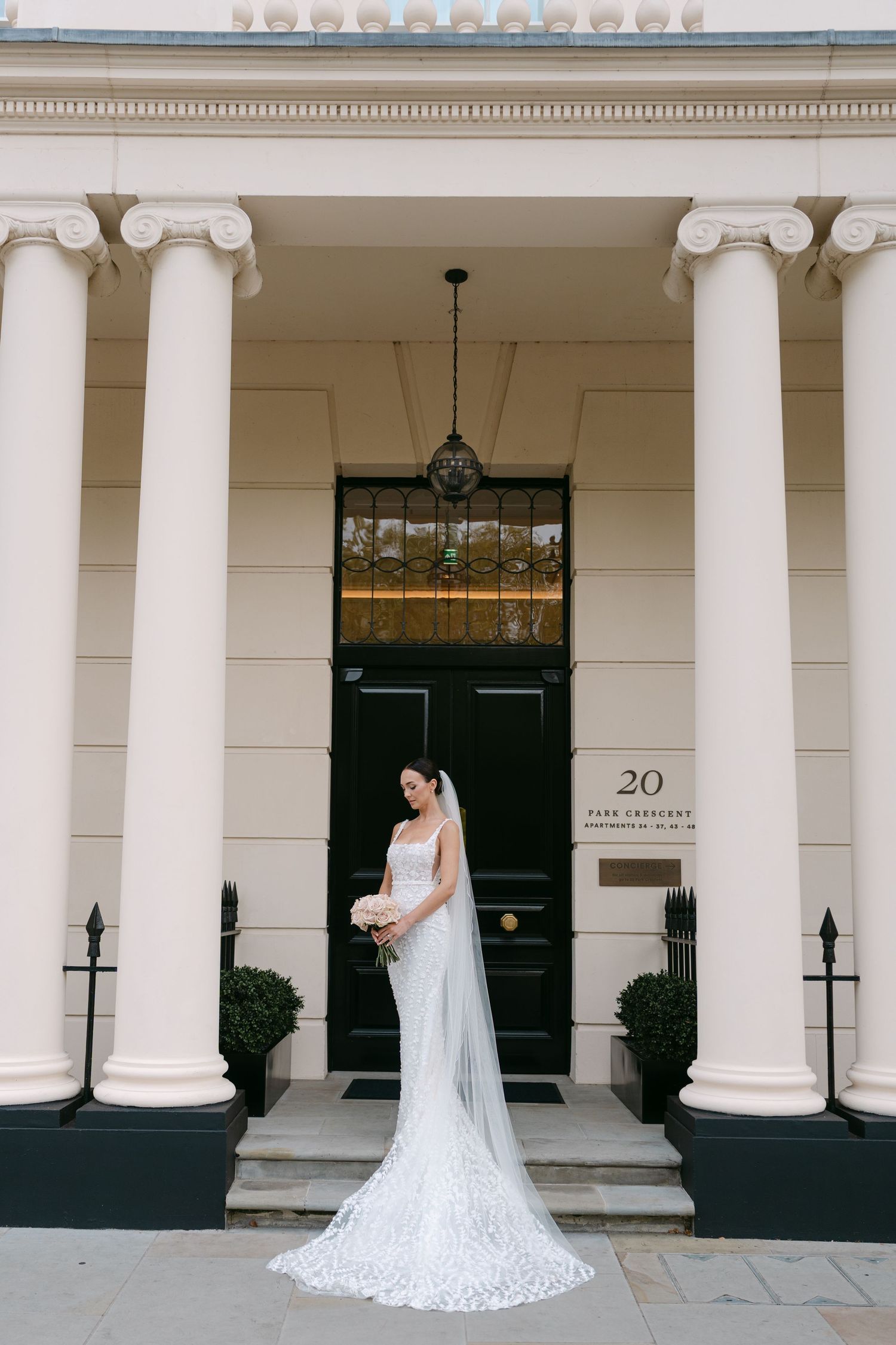 Elegant bridal portrait featuring a long lace train and veil against classic architecture.