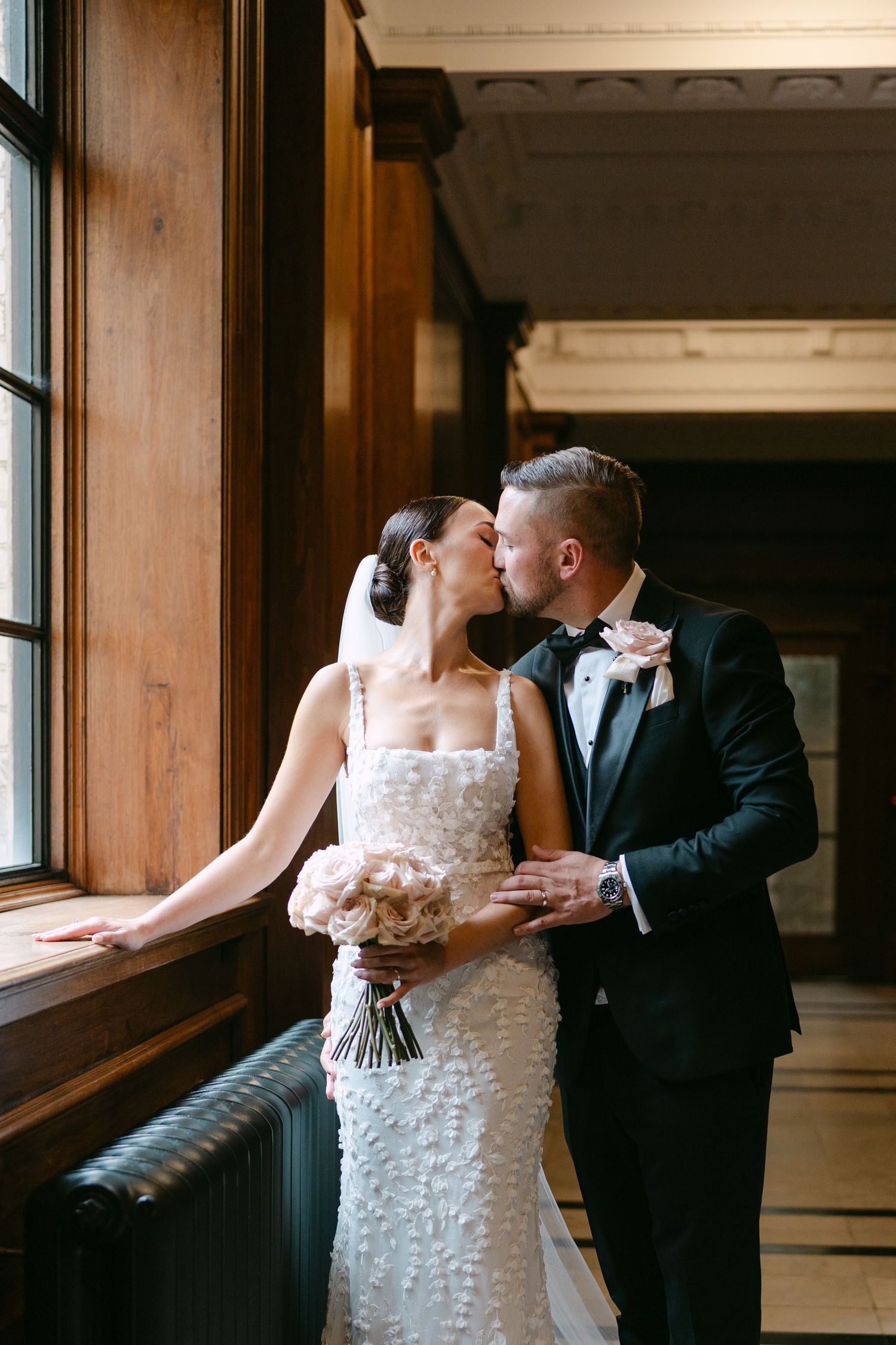 Elegant wedding couple shares an intimate moment by a window in a historic building.