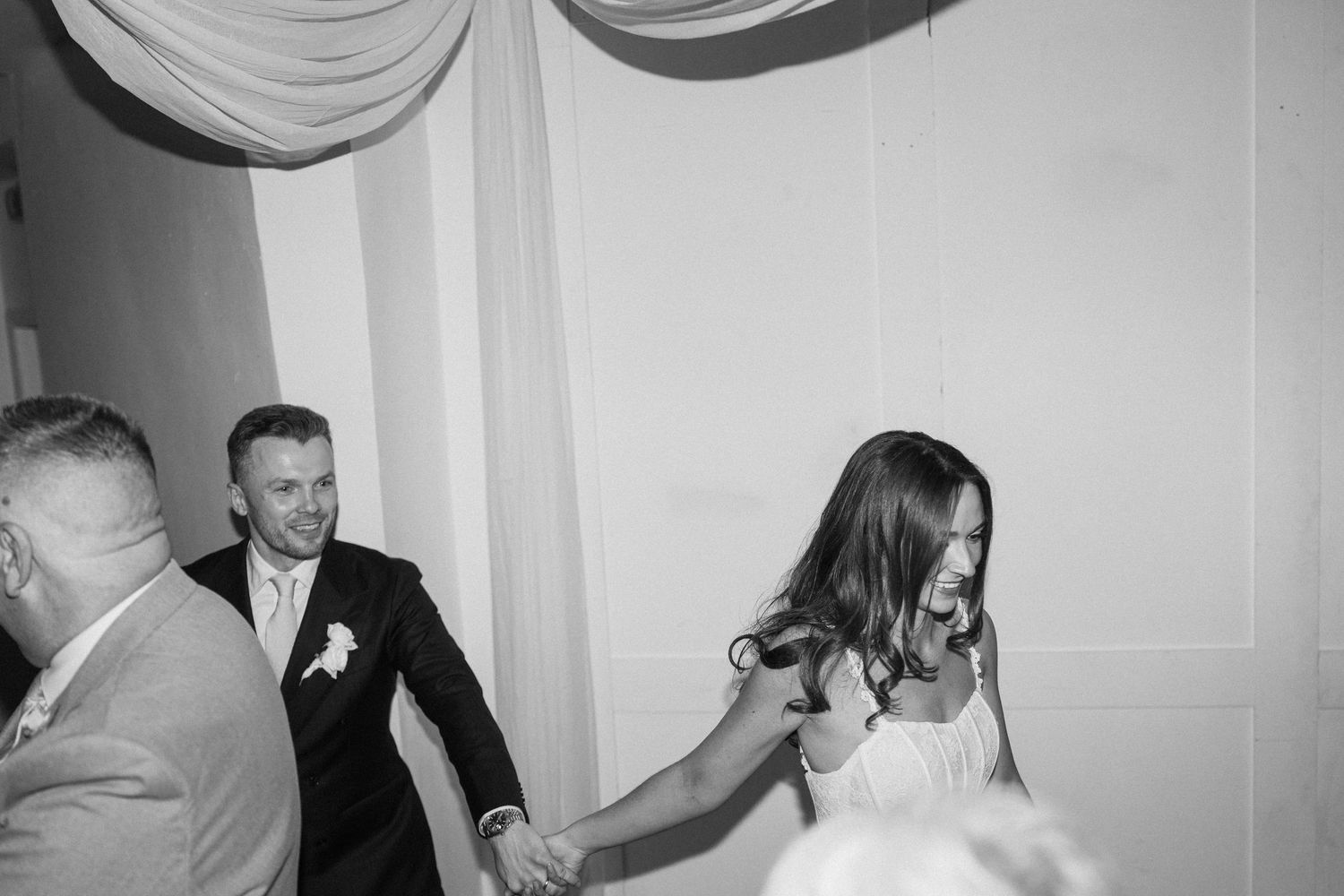 Black and white photo of a bride and groom dancing joyfully at their wedding reception.