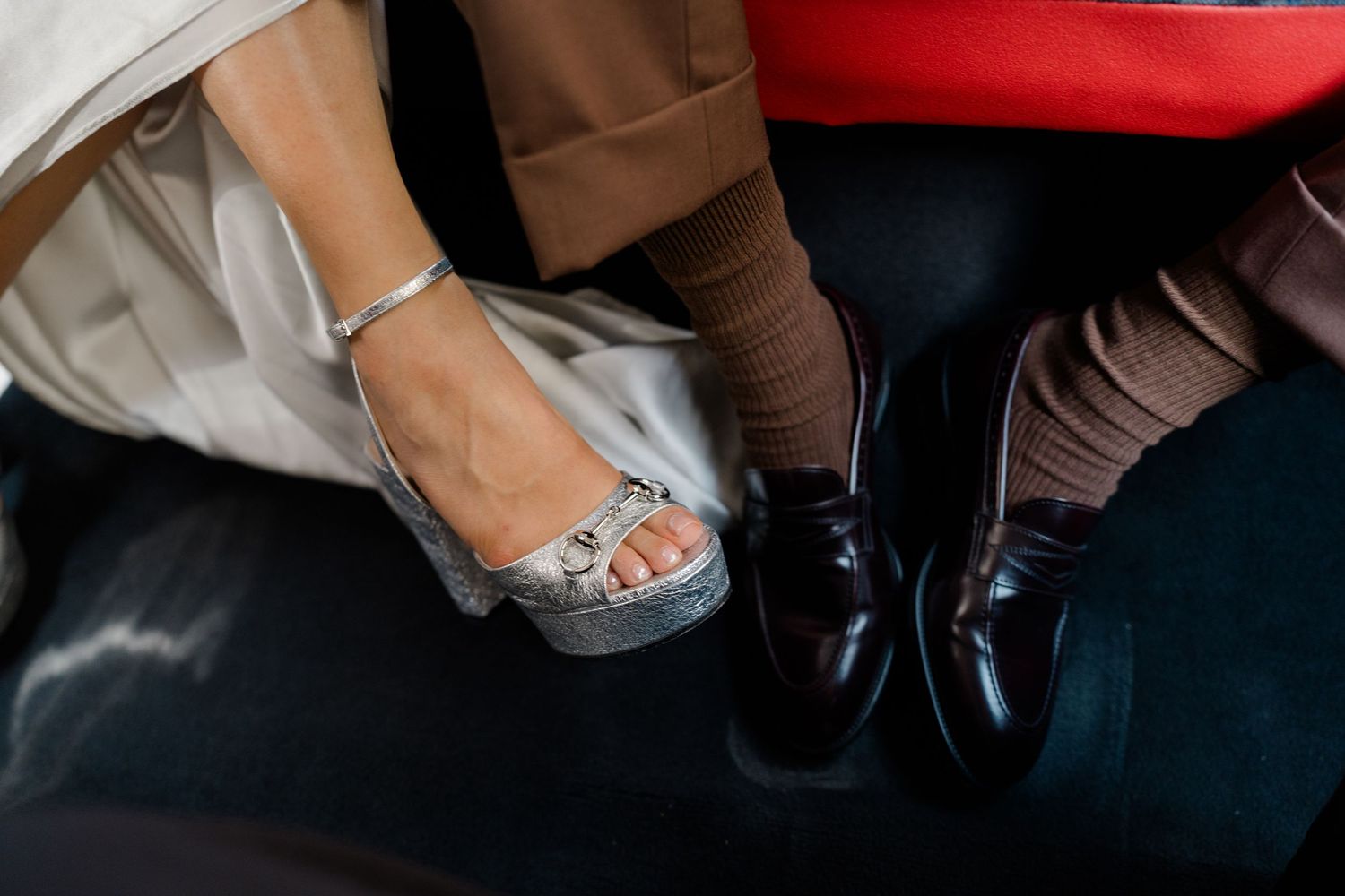 Close-up of bride's silver heeled sandals and groom's brown loafers on wedding day.